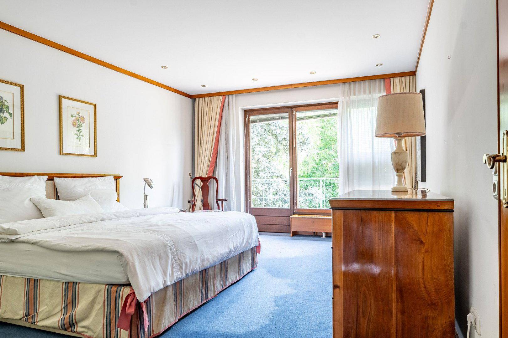 Helles Schlafzimmer mit blauem Teppichboden, Holzakzenten und Zugang zum Balkon.