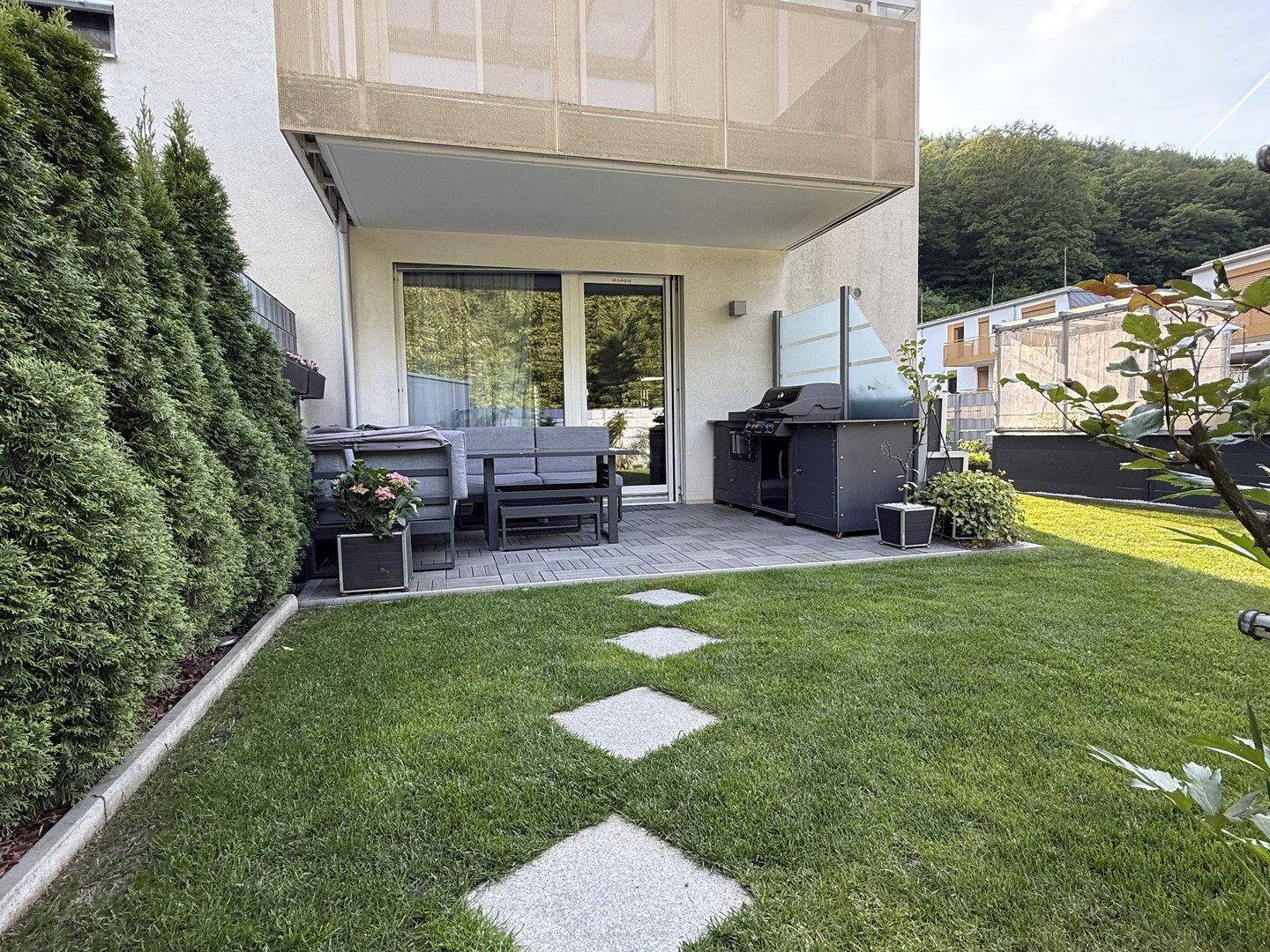 Sonniger Gartenbereich mit Terrasse, Grillplatz und bequemen Outdoor-Sitzmöbeln.