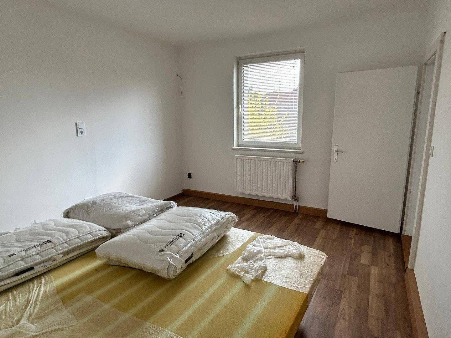 Schlafzimmer mit Laminatboden, Fenster und Tür, die zu einem anderen Raum führt.