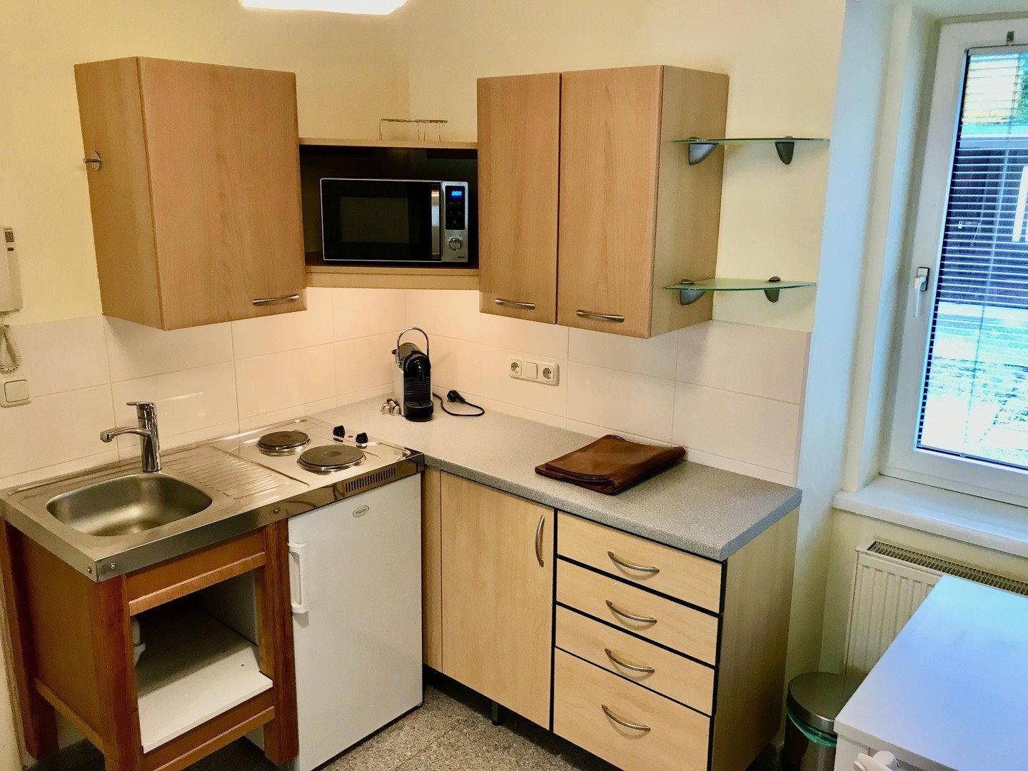Kompakte Küchenzeile mit Holzschränken, Spüle, Mikrowelle und Kühlschrank.