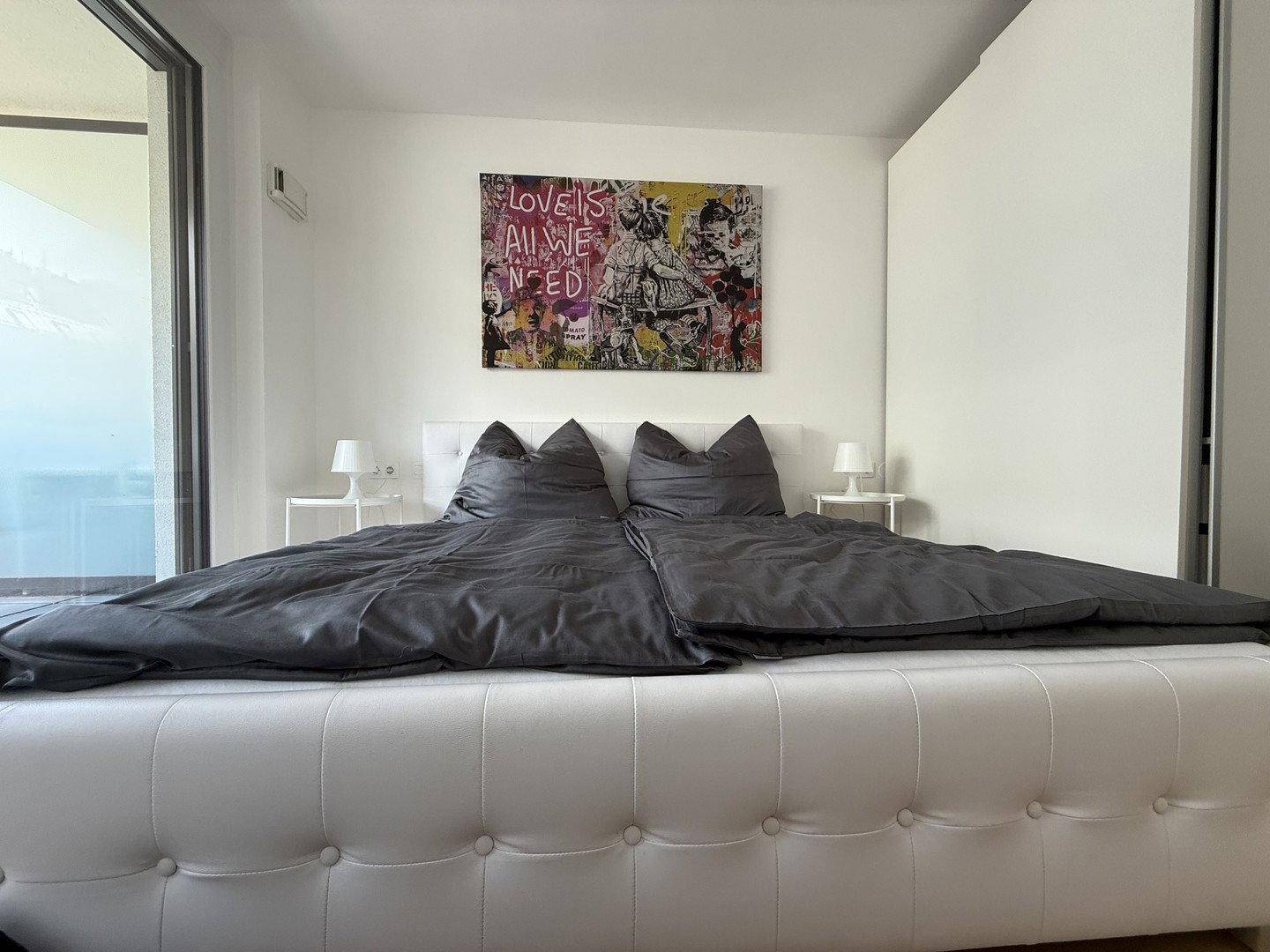 Schlafzimmer mit großem Doppelbett, moderner Kunst an der Wand und Zugang zu einem Außenbereich.