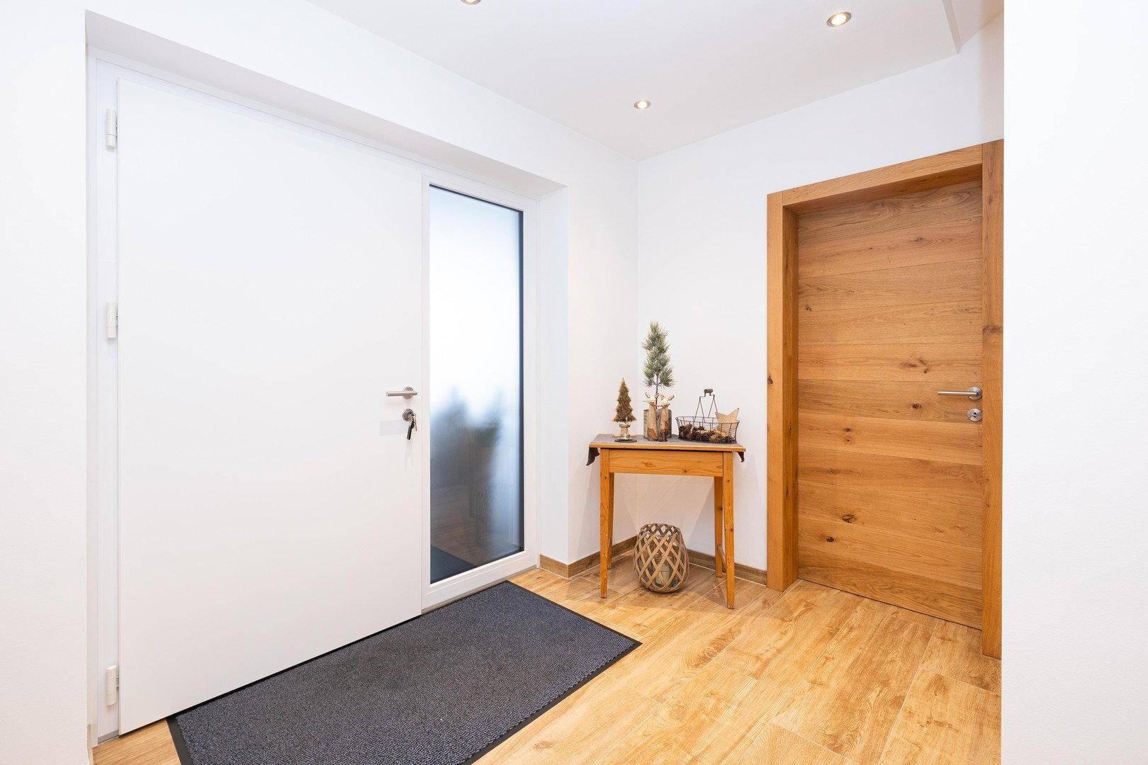 Heller Eingangsbereich mit moderner Haustür, Holztisch und Holzboden.