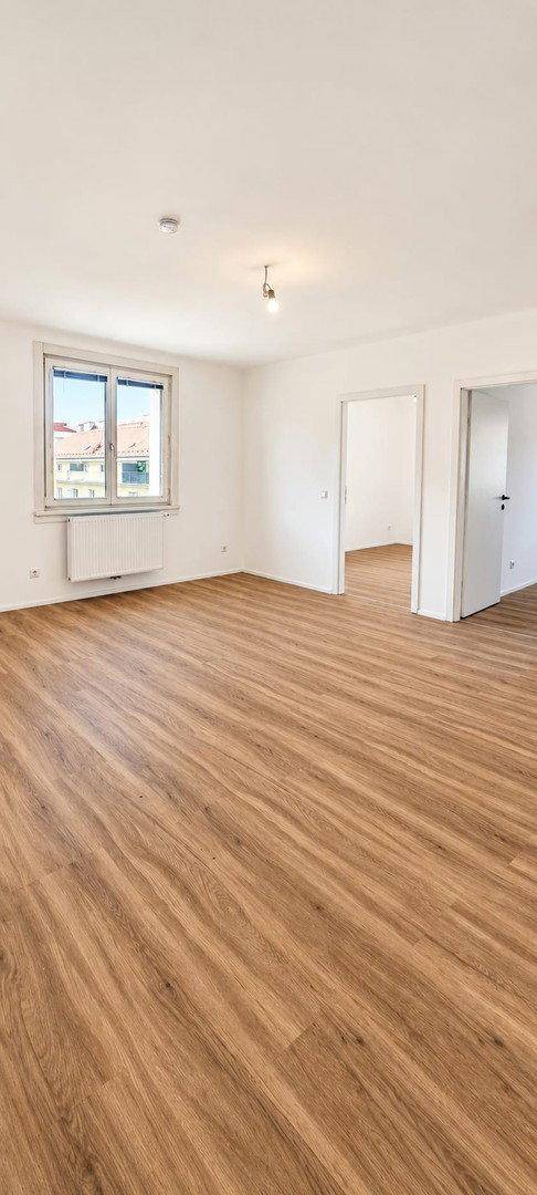 Geräumiges, helles Zimmer mit Laminatboden und großen Fenstern, ideal für Wohn- oder Schlafbereich.