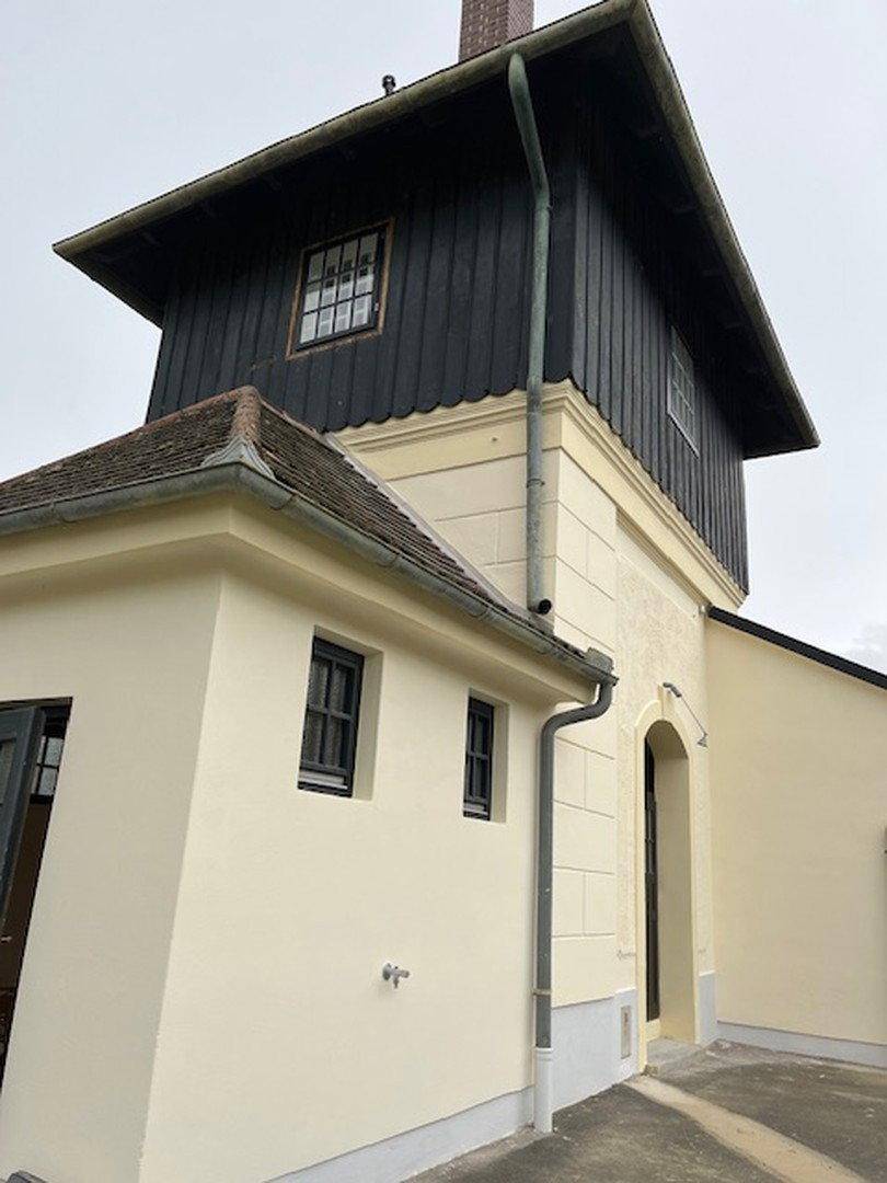 Seitenansicht eines renovierten Gebäudes mit cremefarbener Fassade und dunklem Holzturm.