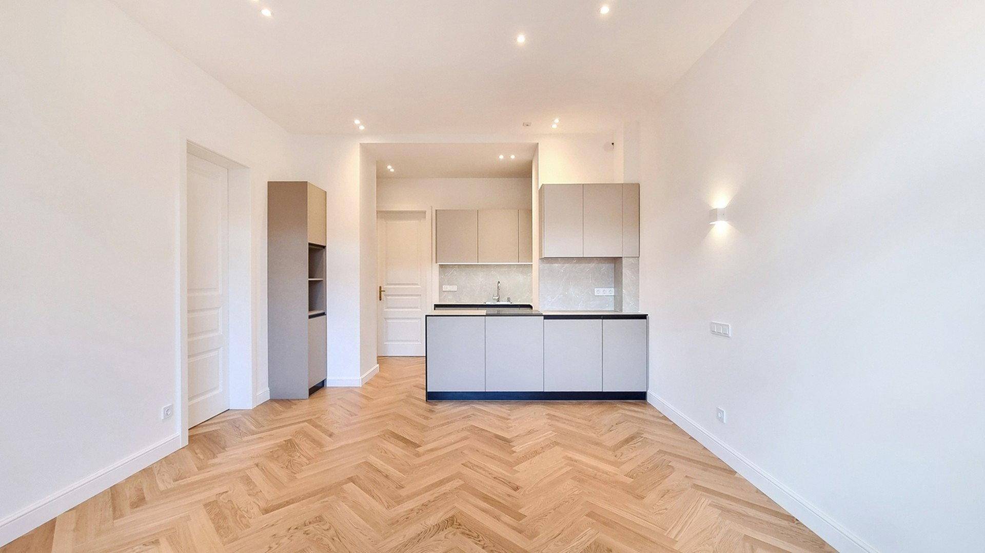 Heller offener Wohnbereich mit moderner Küchenzeile und elegantem Fischgrätparkettboden.