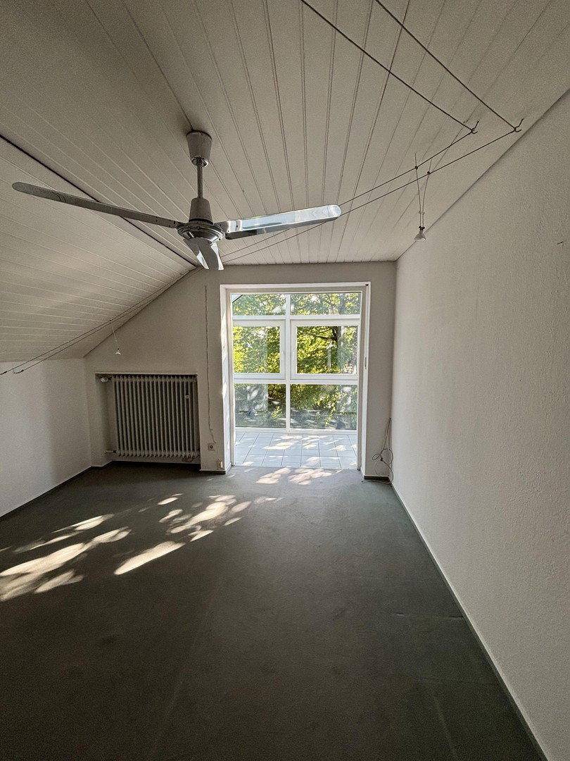Helles Dachzimmer mit Teppichboden, Deckenventilator und Zugang zum Balkon.