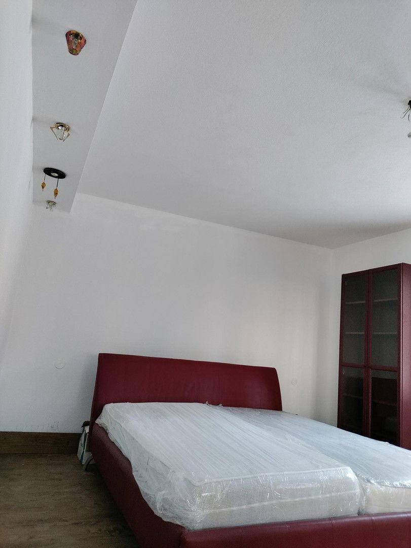 Schlafzimmer mit rotem Bettrahmen, weiß gestrichenen Wänden und minimalistischer Einrichtung.