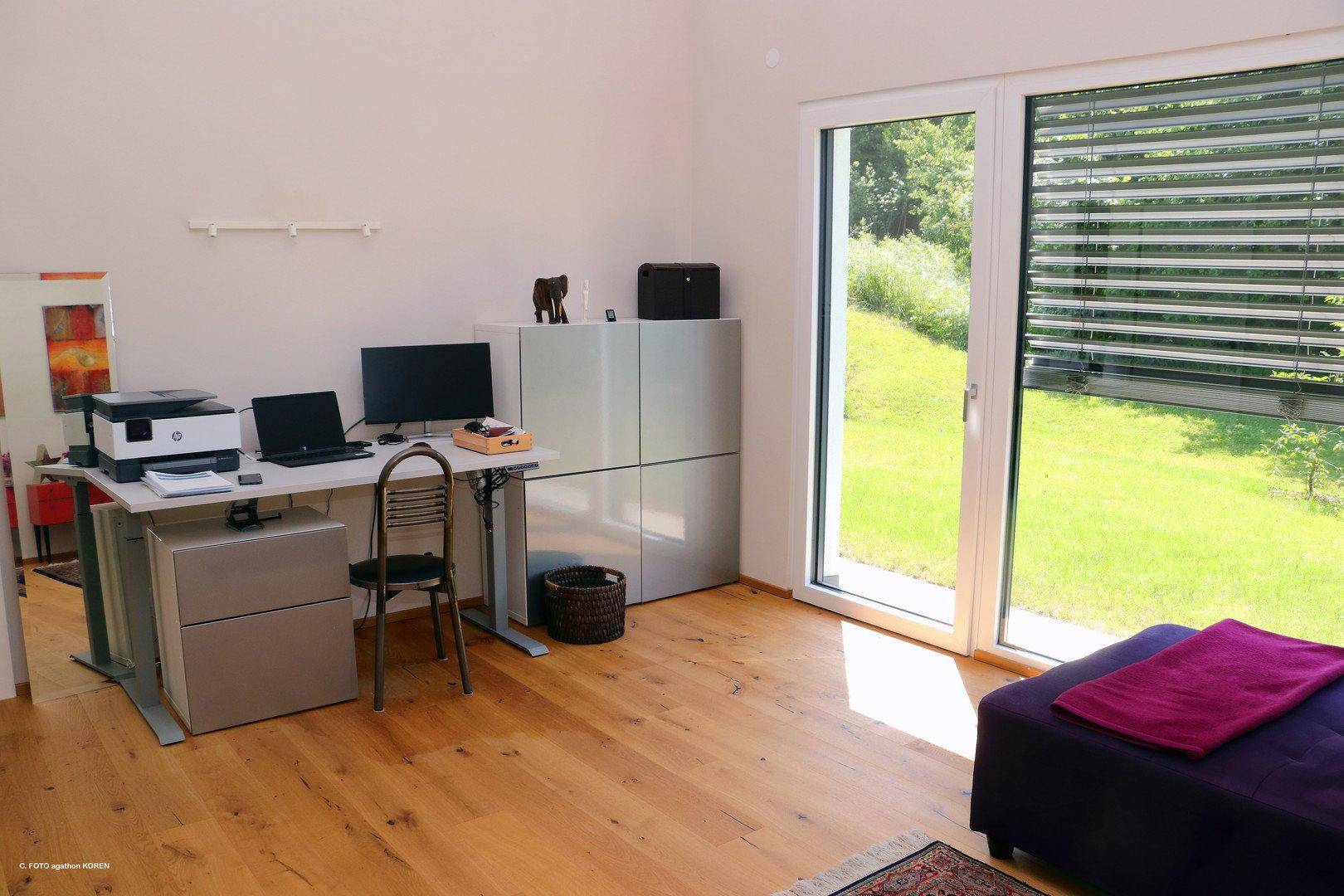 Helles Arbeitszimmer mit Schreibtisch, Büromöbeln und großen Fenstern mit Blick ins Grüne.