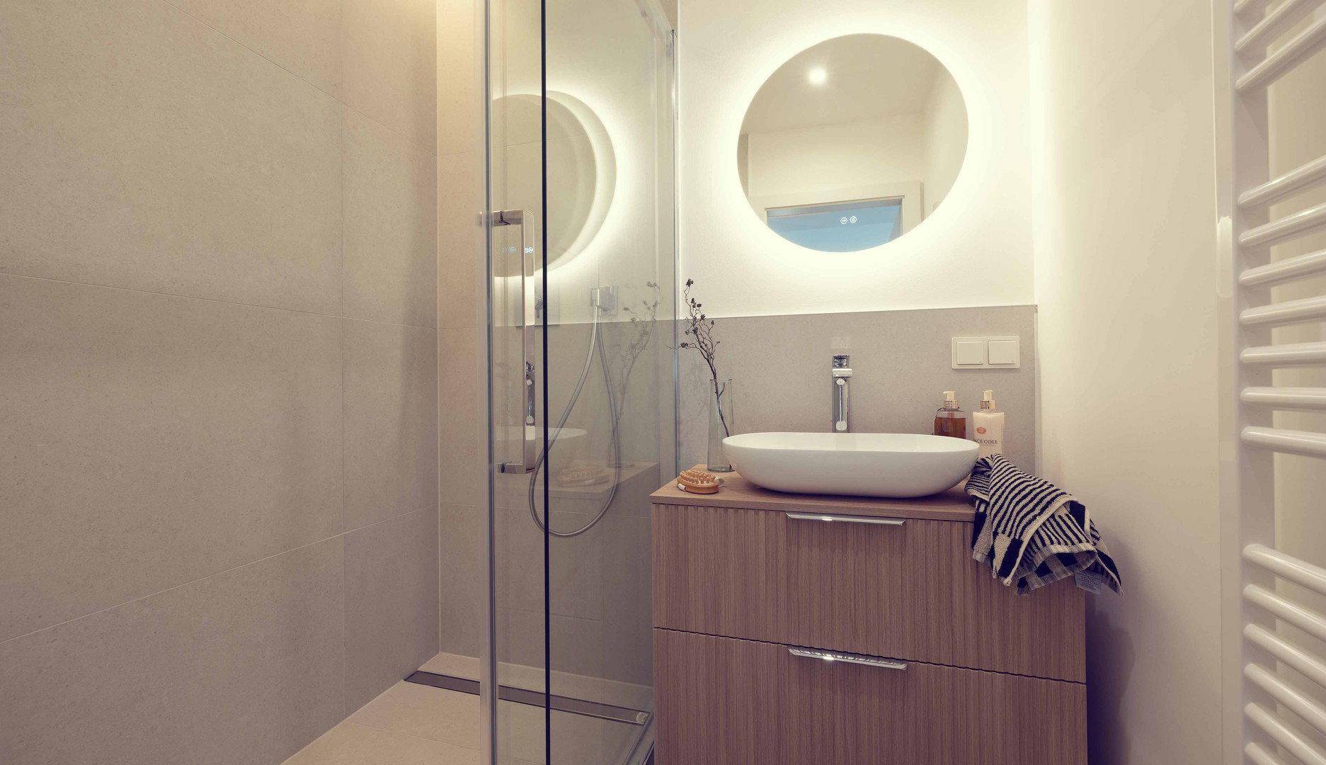Modernes Badezimmer mit begehbarer Dusche, beleuchtetem Spiegel und beheiztem Handtuchhalter.