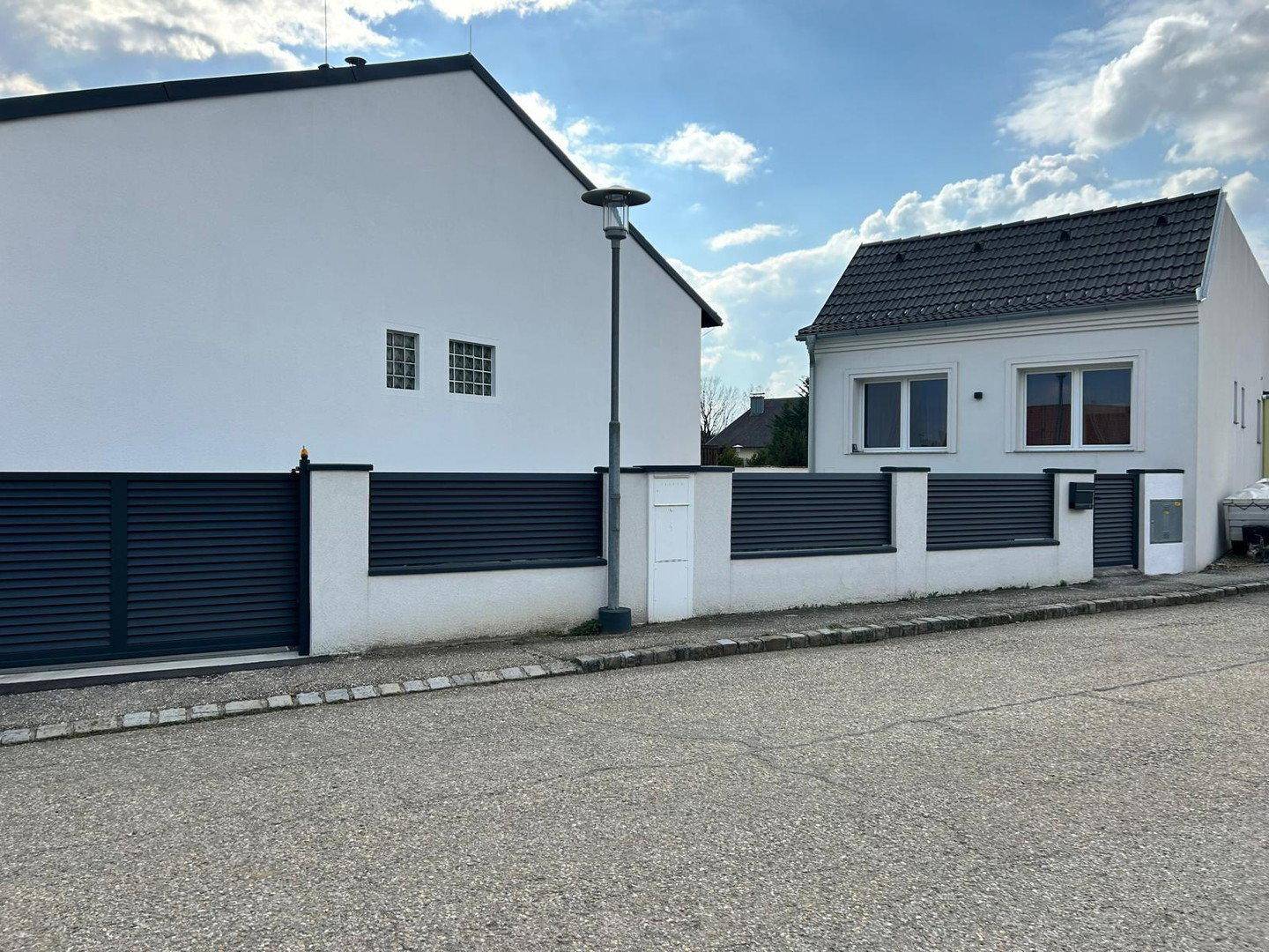 Straßenansicht des Anwesens mit weißem Gebäude und modernem schwarzem Zaun.