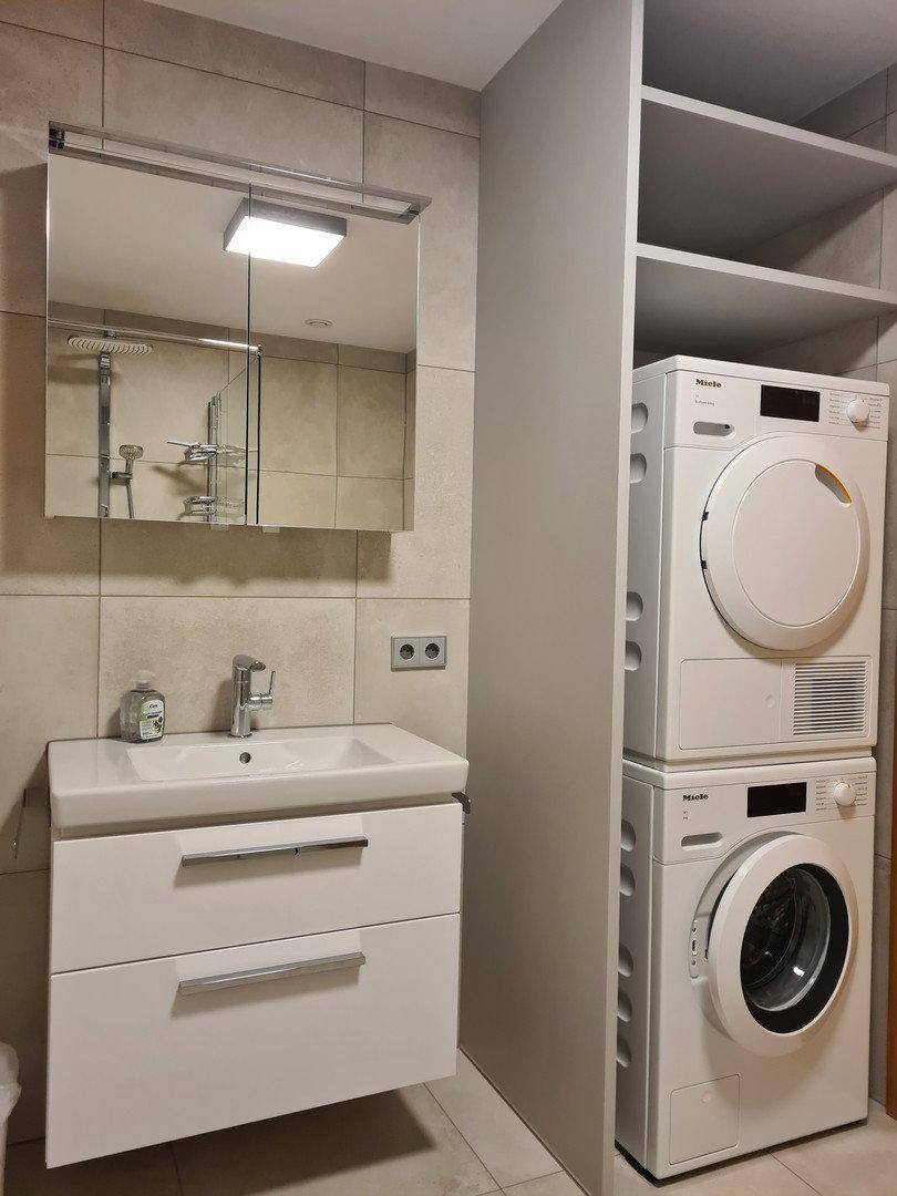 Badezimmer mit Waschbecken, Spiegelschrank und integriertem Waschmaschinen-Trockner-Turm.