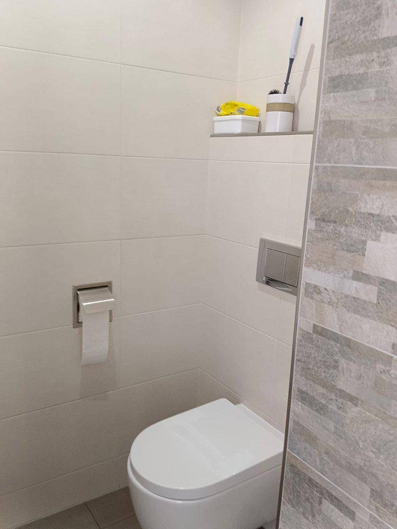 Modernes WC mit wandhängender Toilette und hellen Fliesen in einem Badezimmer.