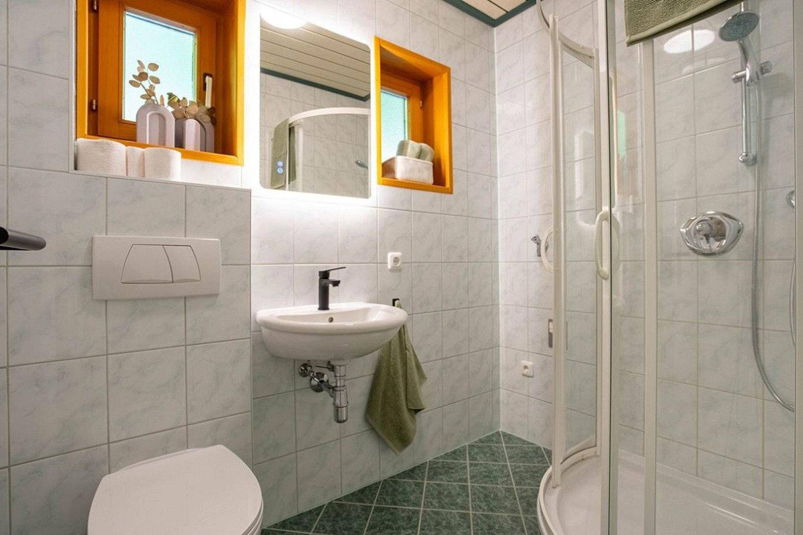 Gefliestes Badezimmer mit Dusche, WC, Waschbecken und Fenster für Tageslicht.