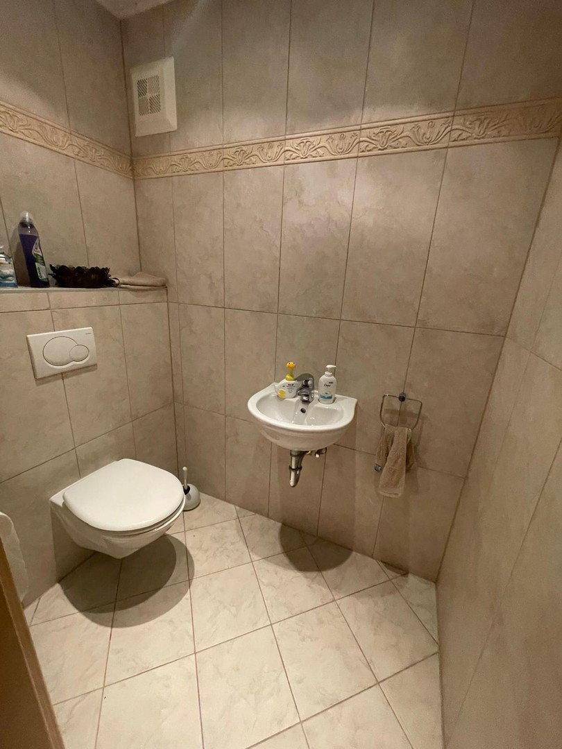 Kleines Gäste-WC mit Wand-WC, Waschbecken und beigefarbenen Fliesen an Wänden und Boden.