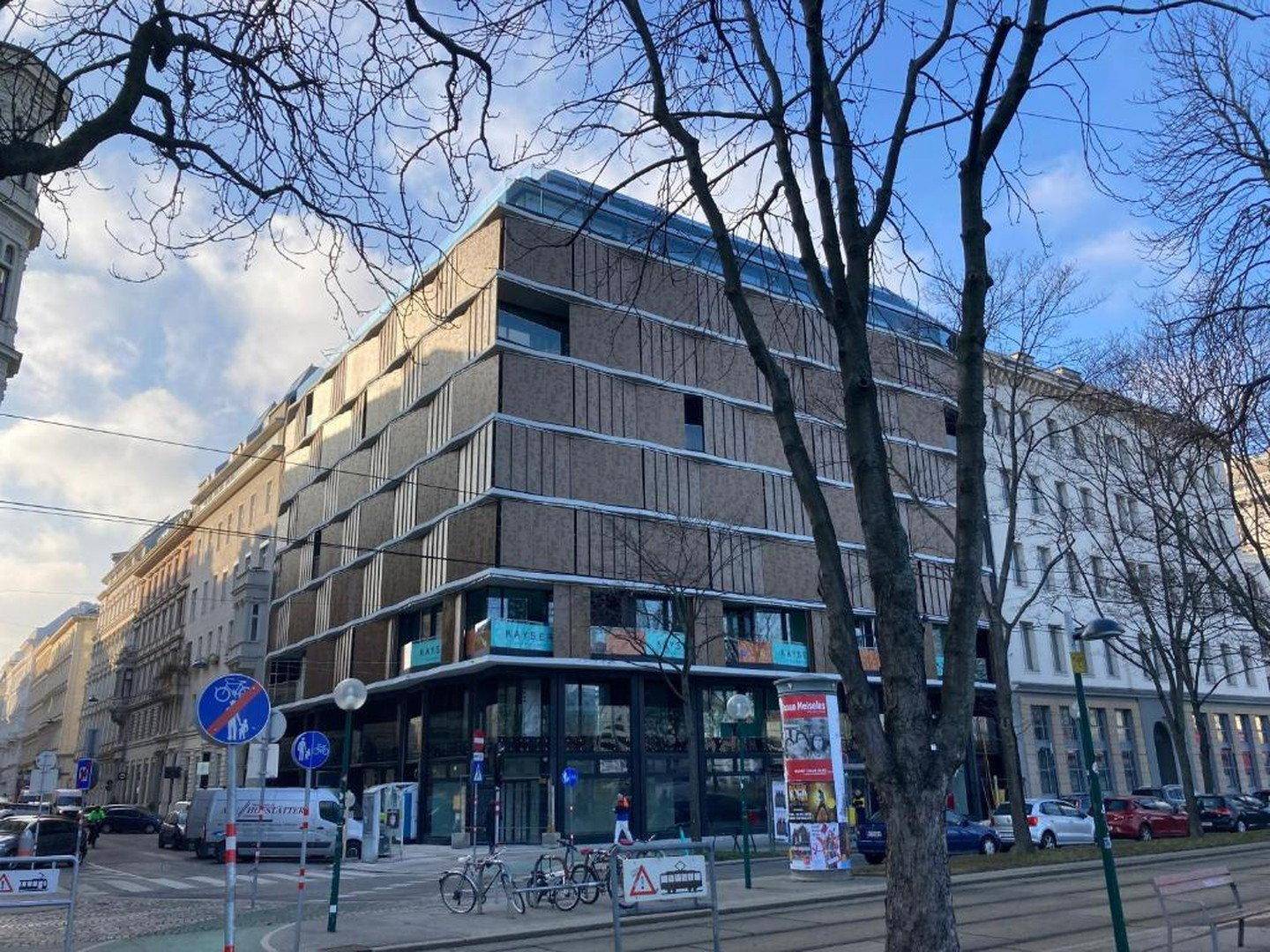 Moderne Gebäudefassade mit großen Fenstern und Geschäften im Erdgeschoss an einer Straßenecke.