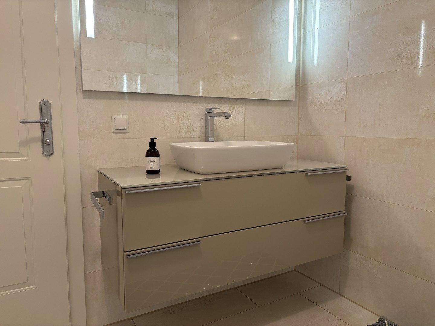 Modernes Badezimmer mit beigen Fliesen, Aufsatzwaschbecken und schwebendem Waschtisch.