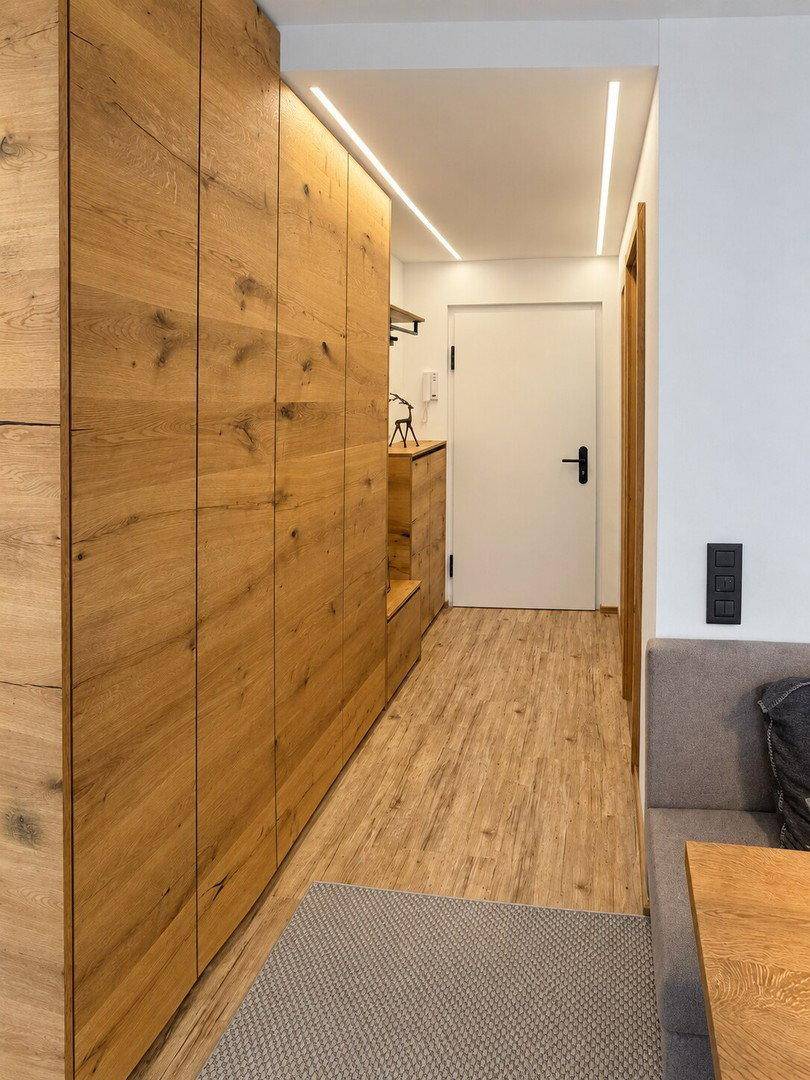 Heller Flur mit integrierten Holzschränken und moderner Beleuchtung, die zum Eingang führt.