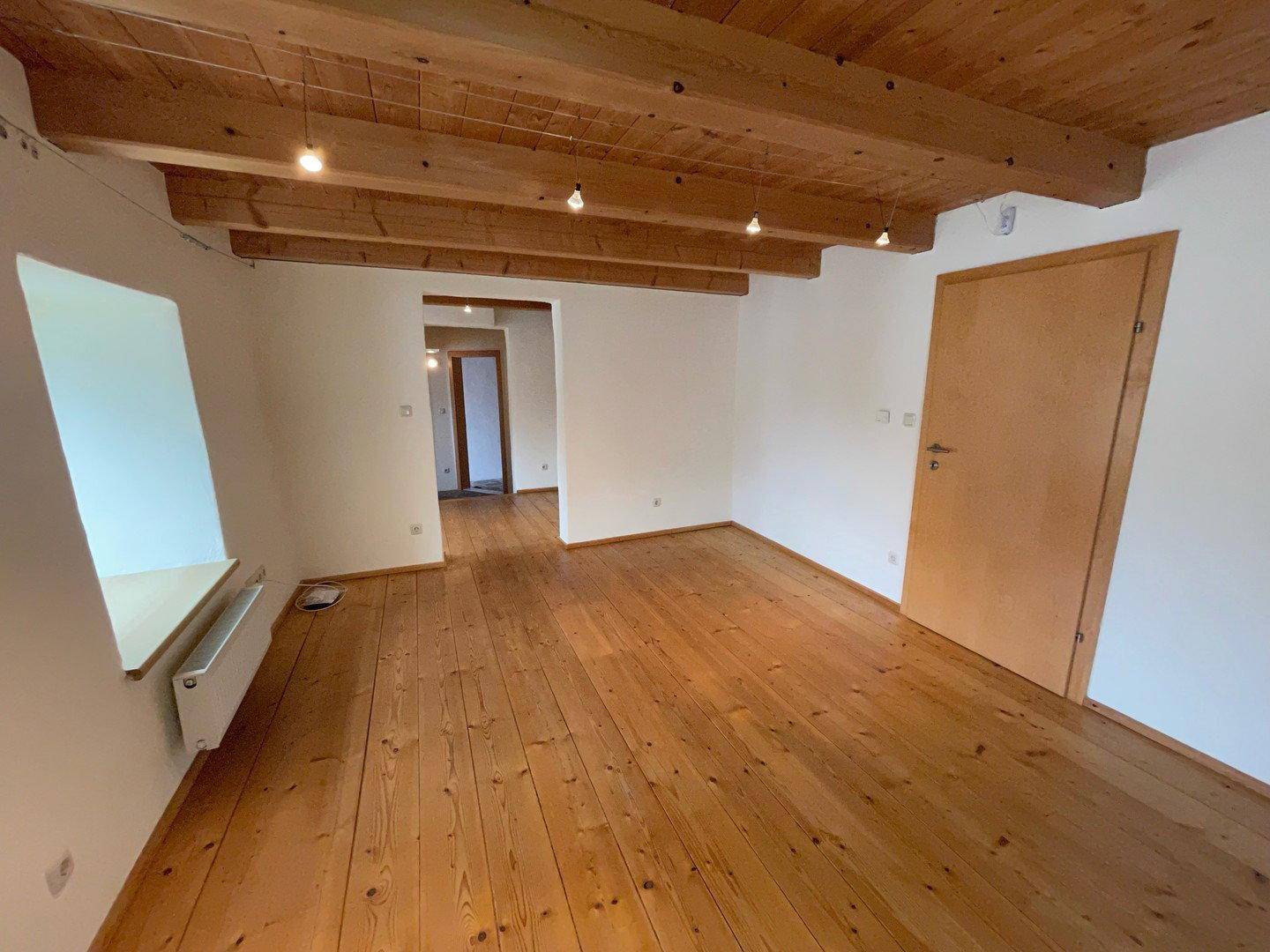 Helles Wohnzimmer mit Holzdielenboden und freiliegenden Deckenbalken, Blick in den Flur.