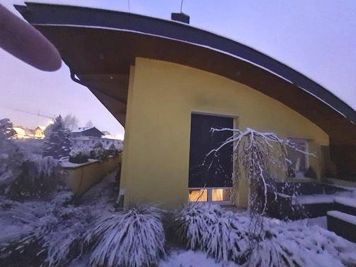 Modernes Haus mit geschwungenem Dach und gelber Fassade, umgeben von schneebedeckter Winterlandschaft.