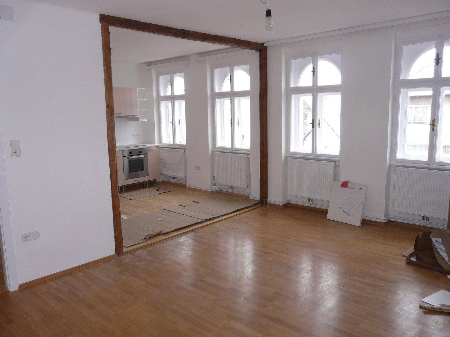 Geräumiger Wohnbereich mit Holzboden und großen Fenstern, angrenzend an die Küche.