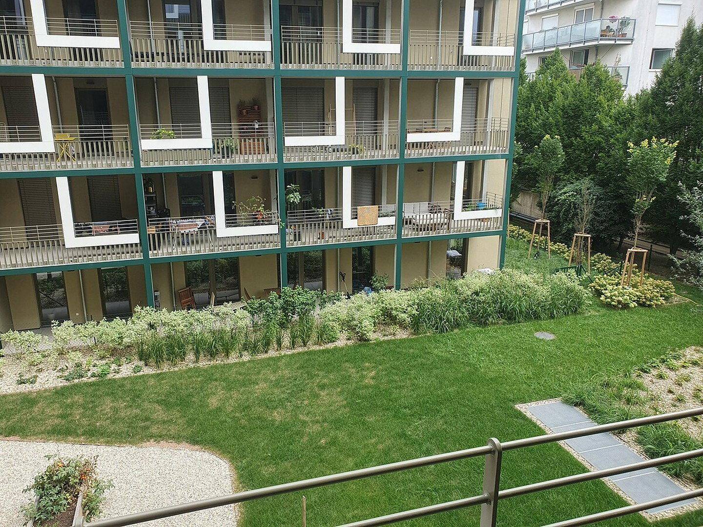 Außenansicht eines Wohngebäudes mit vielen Balkonen und Blick auf einen gepflegten Garten.
