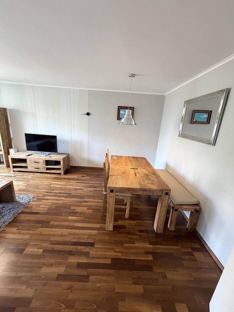 Essbereich im Wohnzimmer mit Holztisch, Bank und einem großen Wandspiegel.