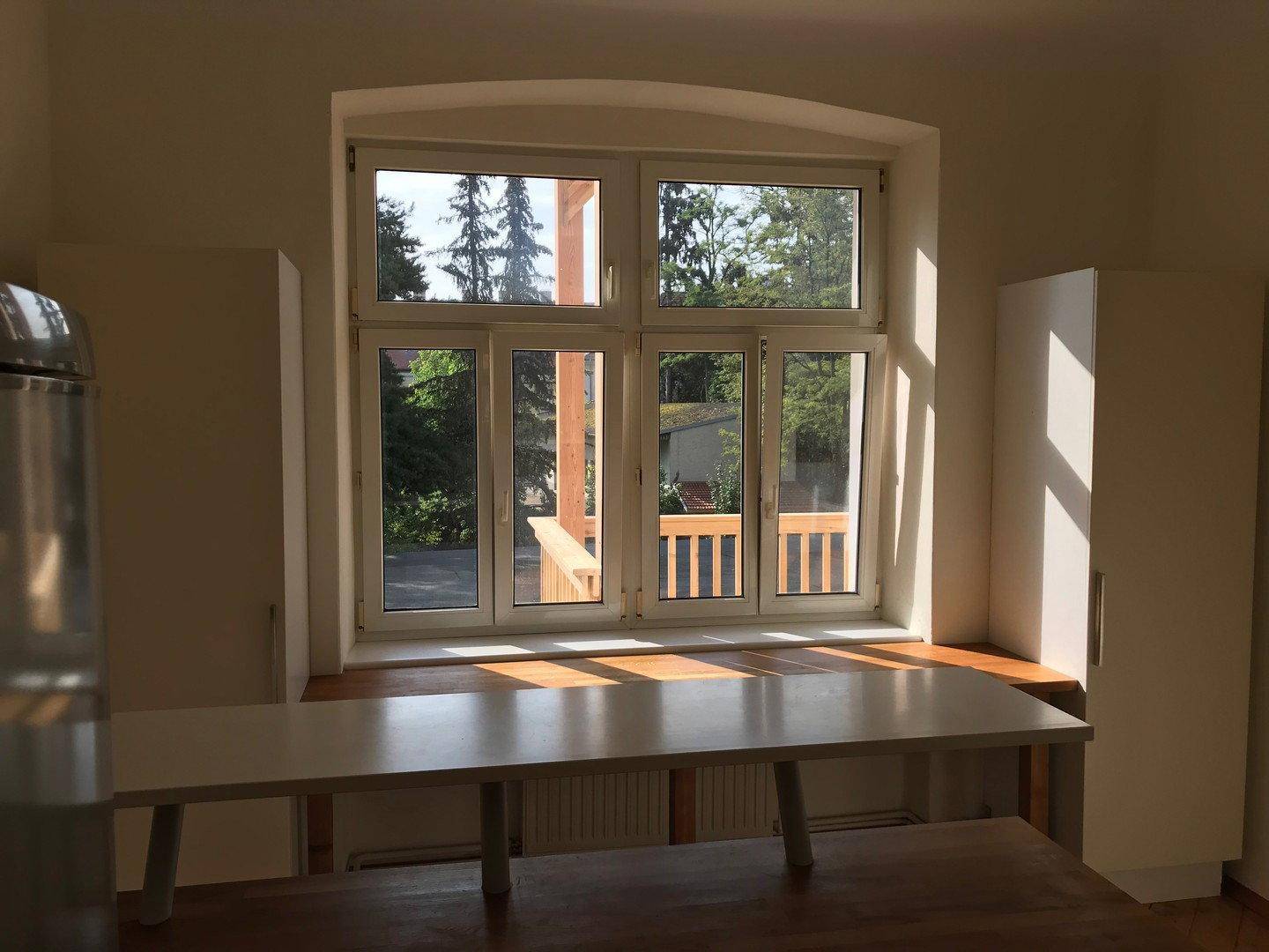 Heller Küchenbereich mit großem Fenster, das einen Blick ins Grüne und auf den Balkon bietet.
