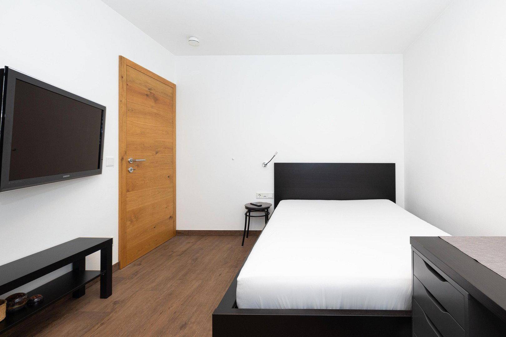 Schlafzimmer mit Einzelbett, Fernseher und Holzboden, ideal als Gästezimmer.