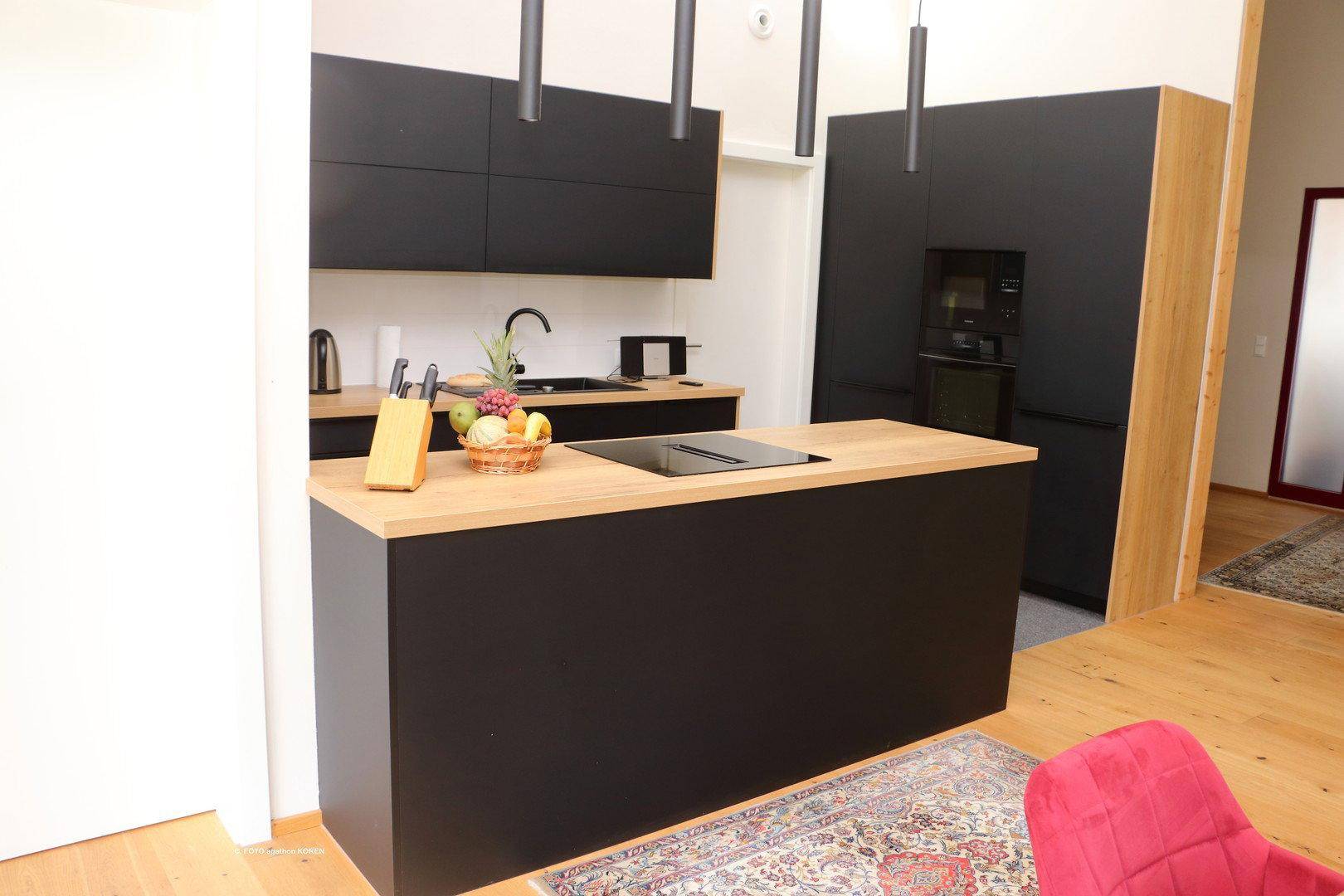 Moderne schwarze Einbauküche mit Kochinsel, Holz-Arbeitsplatte und Induktionskochfeld.
