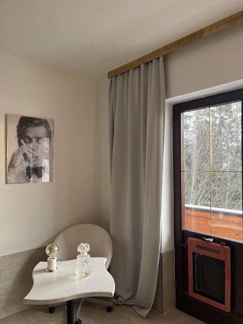 Helle Zimmerecke mit Balkontür, Vorhängen und einem kleinen Tisch mit Stuhl.