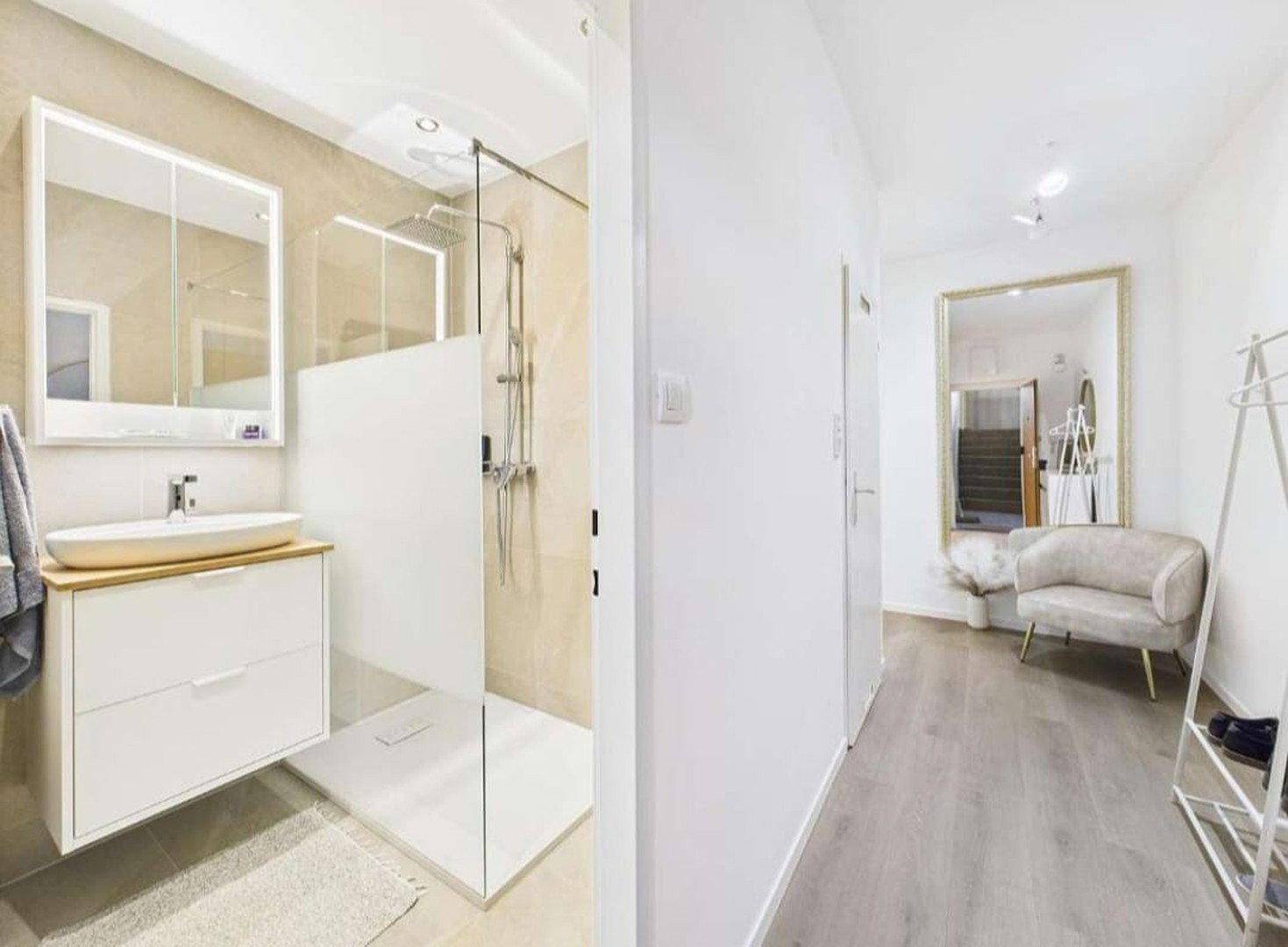 Eingangsbereich mit Spiegel und Zugang zu einem modernen Badezimmer mit Dusche.