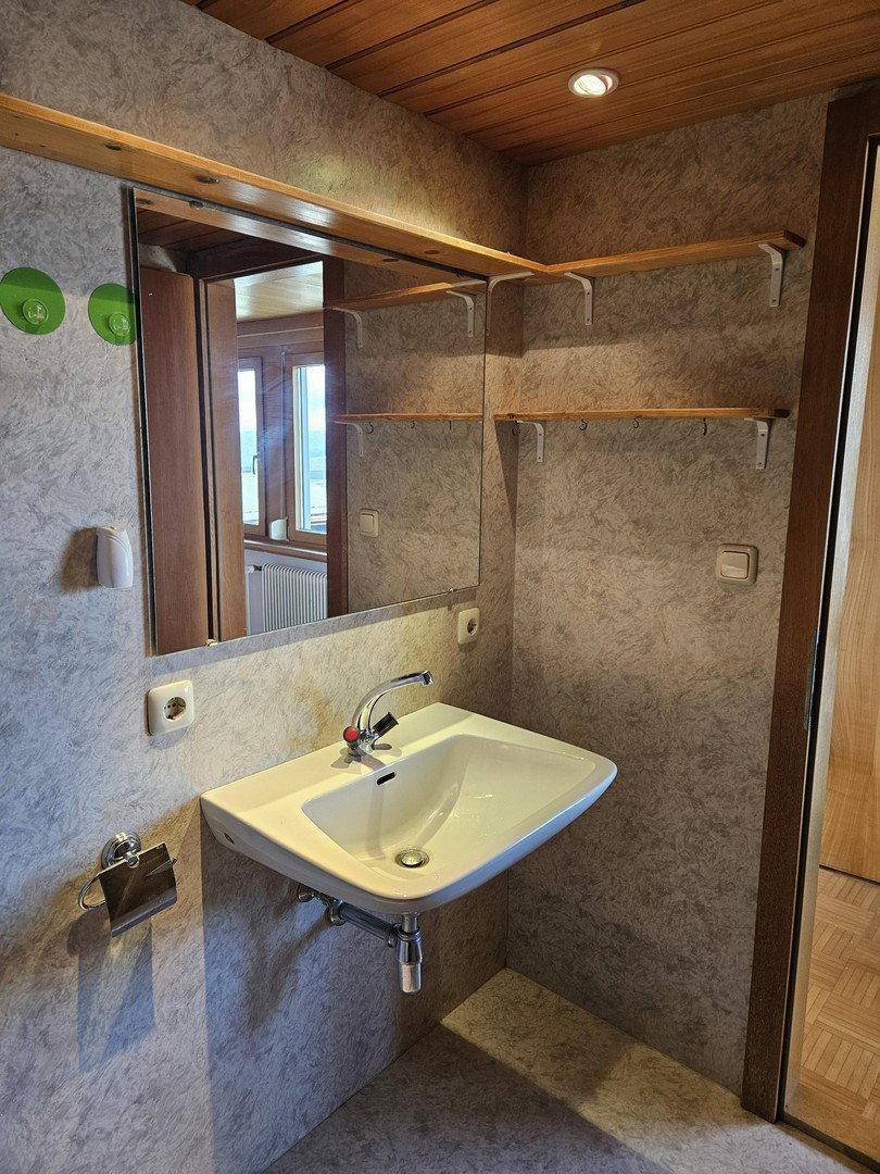 Badezimmer mit Waschbecken, Spiegel und Ablageflächen, passend zur Holzdecke.