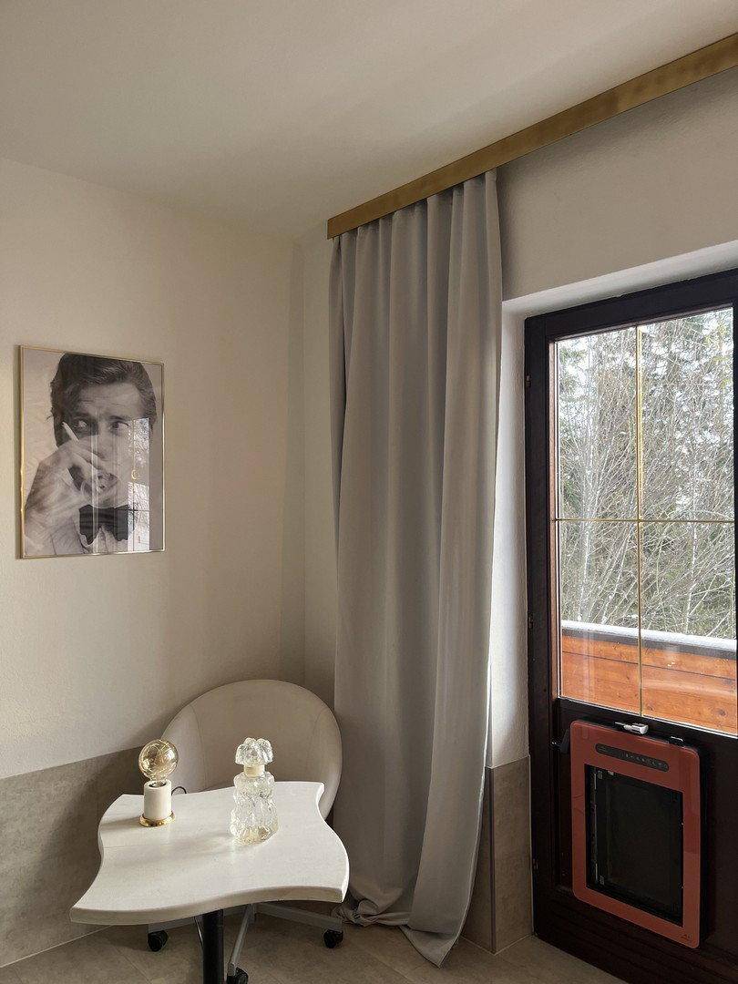 Gemütliche Ecke mit kleinem Tisch, Stuhl und Zugang zu einem Balkon mit Winterlandschaft.