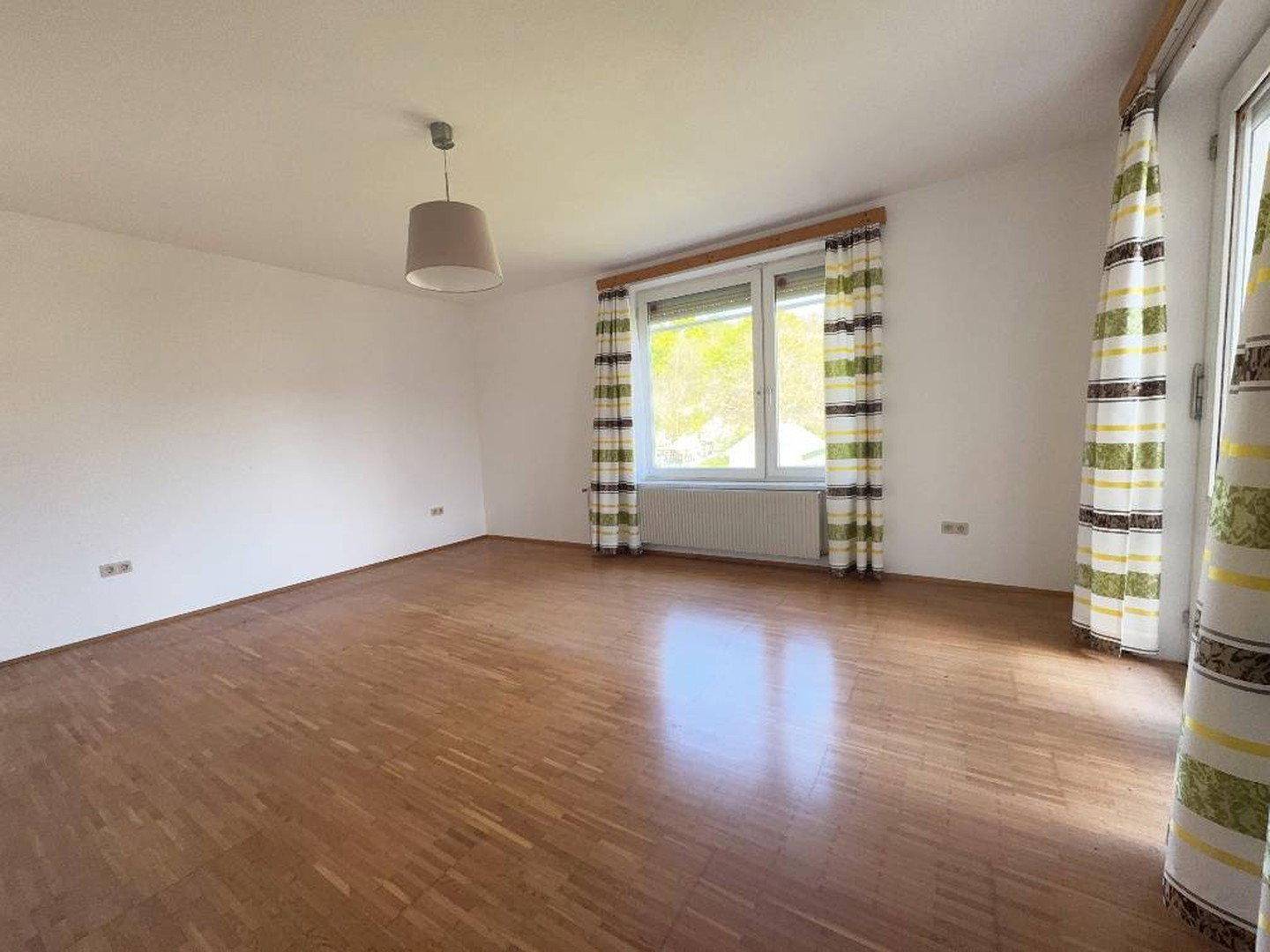 Helles Schlafzimmer mit Holzfußboden und Fenster mit Blick ins Grüne.