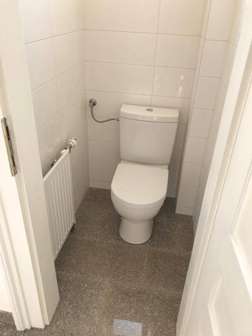 Separate Toilette mit WC und Heizkörper, vollständig mit weißen Fliesen ausgestattet.