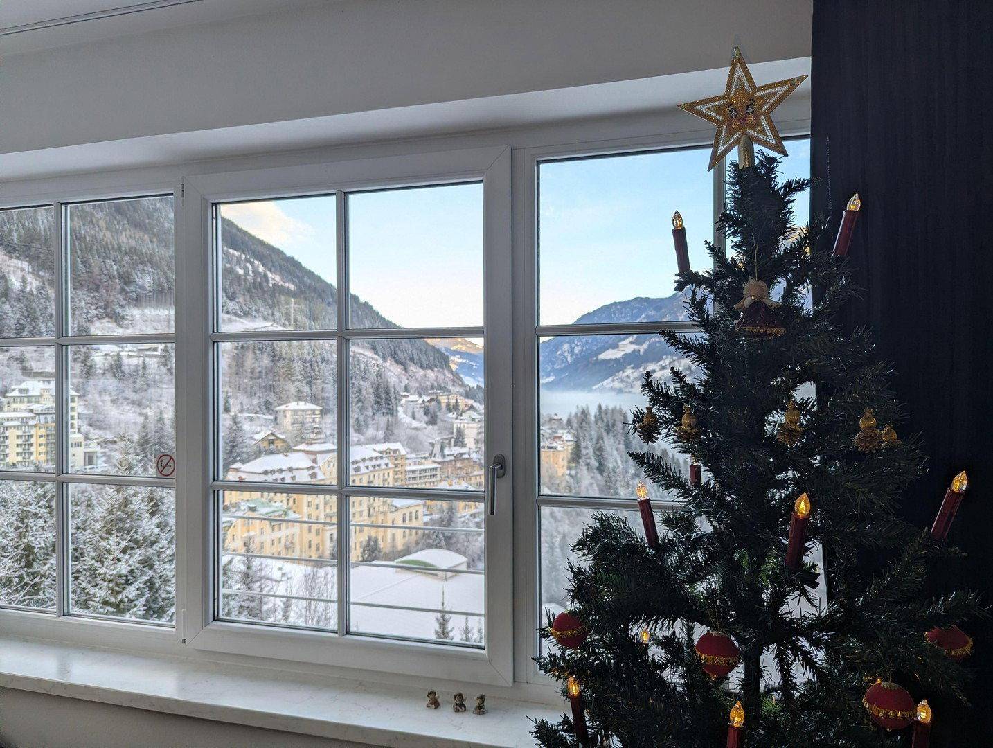 Fenster mit Blick auf eine verschneite Berglandschaft und einen festlich geschmückten Weihnachtsbaum.