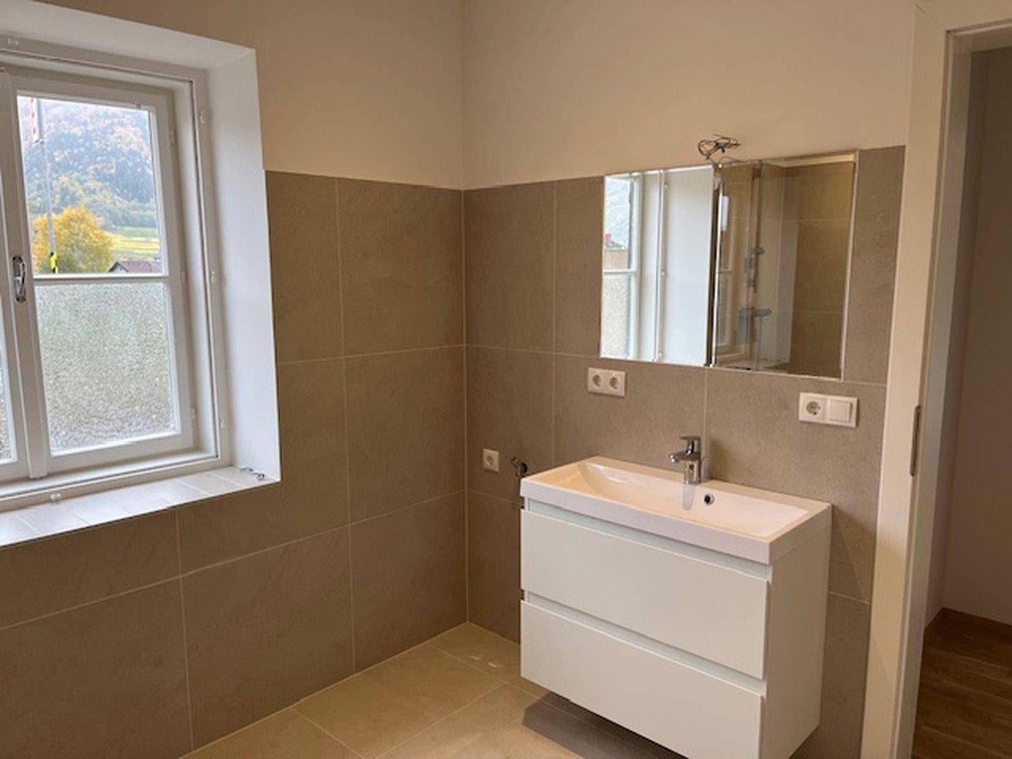 Modernes Badezimmer mit beigefarbenen Fliesen, schwebendem Waschtisch und Spiegelschrank.