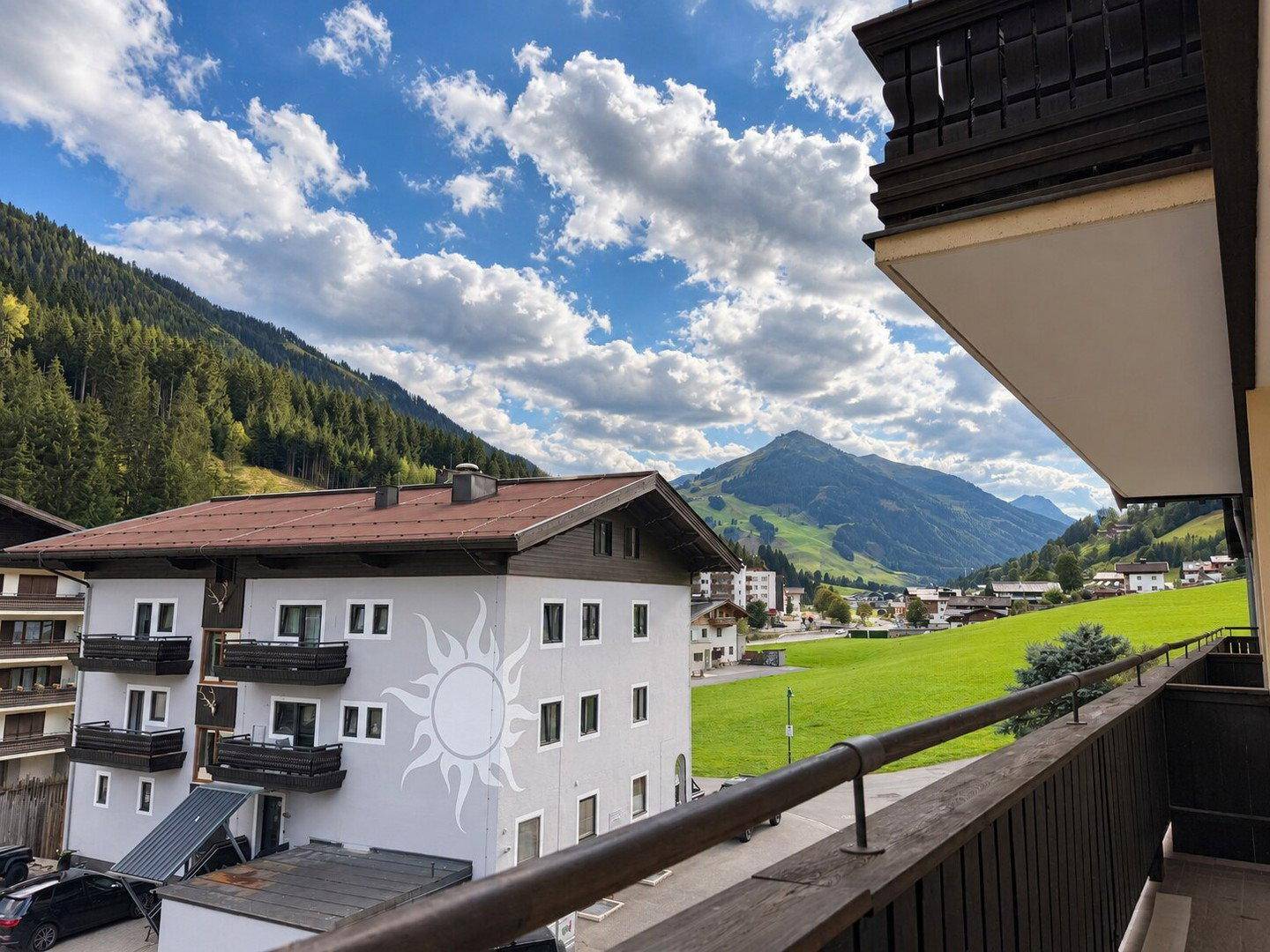 Balkon mit weitem Blick auf die umliegende Berglandschaft und ein Gebäude mit Sonnenmotiv.
