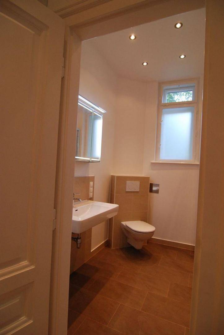 Kleines WC mit Waschbecken, Wand-WC, Spiegelschrank und beigefarbenen Fliesen.