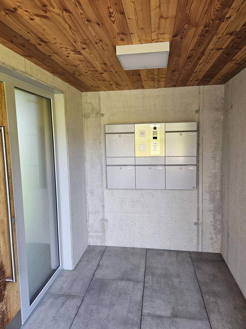 Moderner Eingangsbereich mit Holzdecke, Fliesenboden und Briefkastenanlage mit Gegensprechanlage.