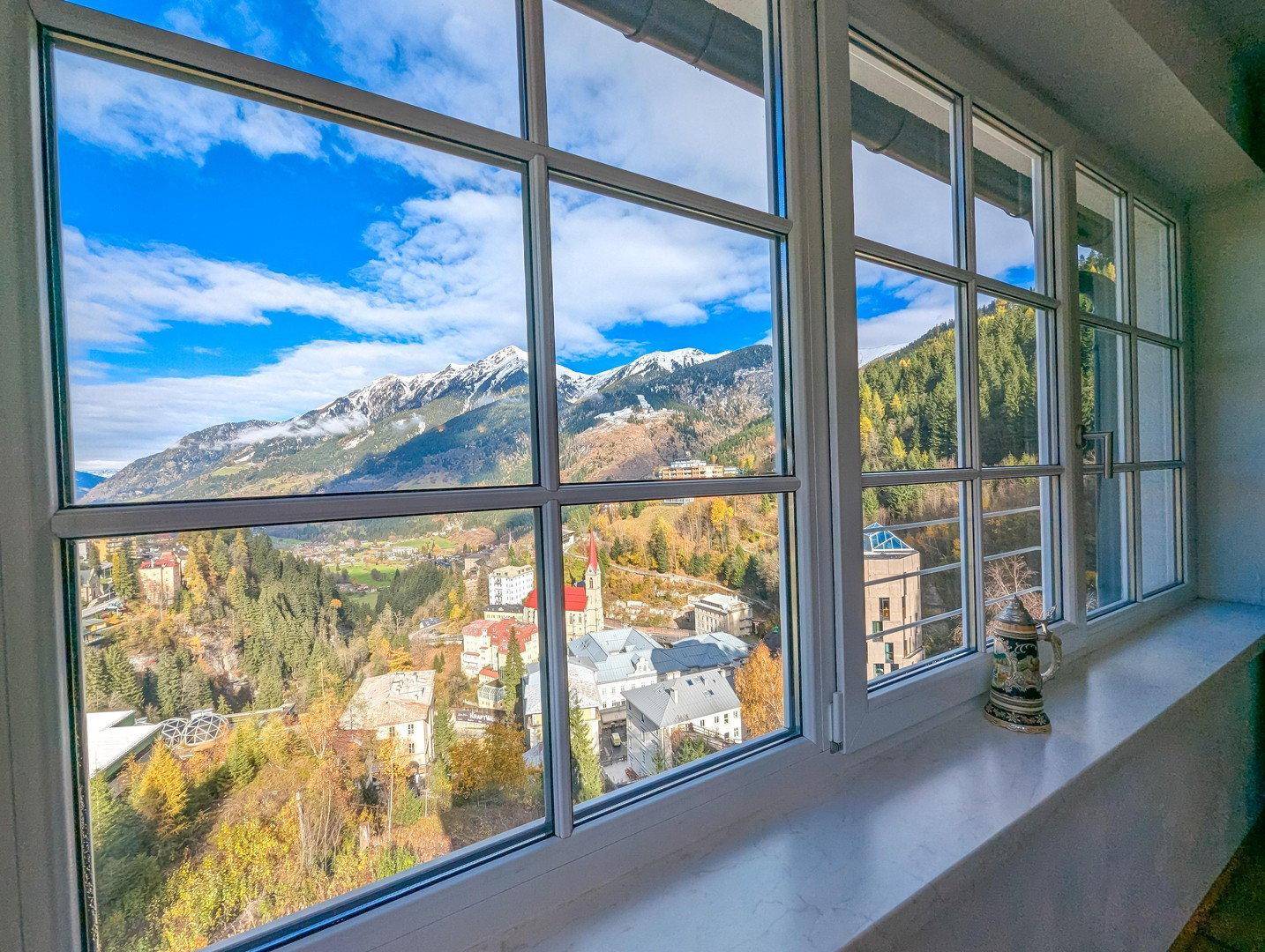 Fenster mit Panoramablick auf die herbstliche Berglandschaft und das malerische Dorf.