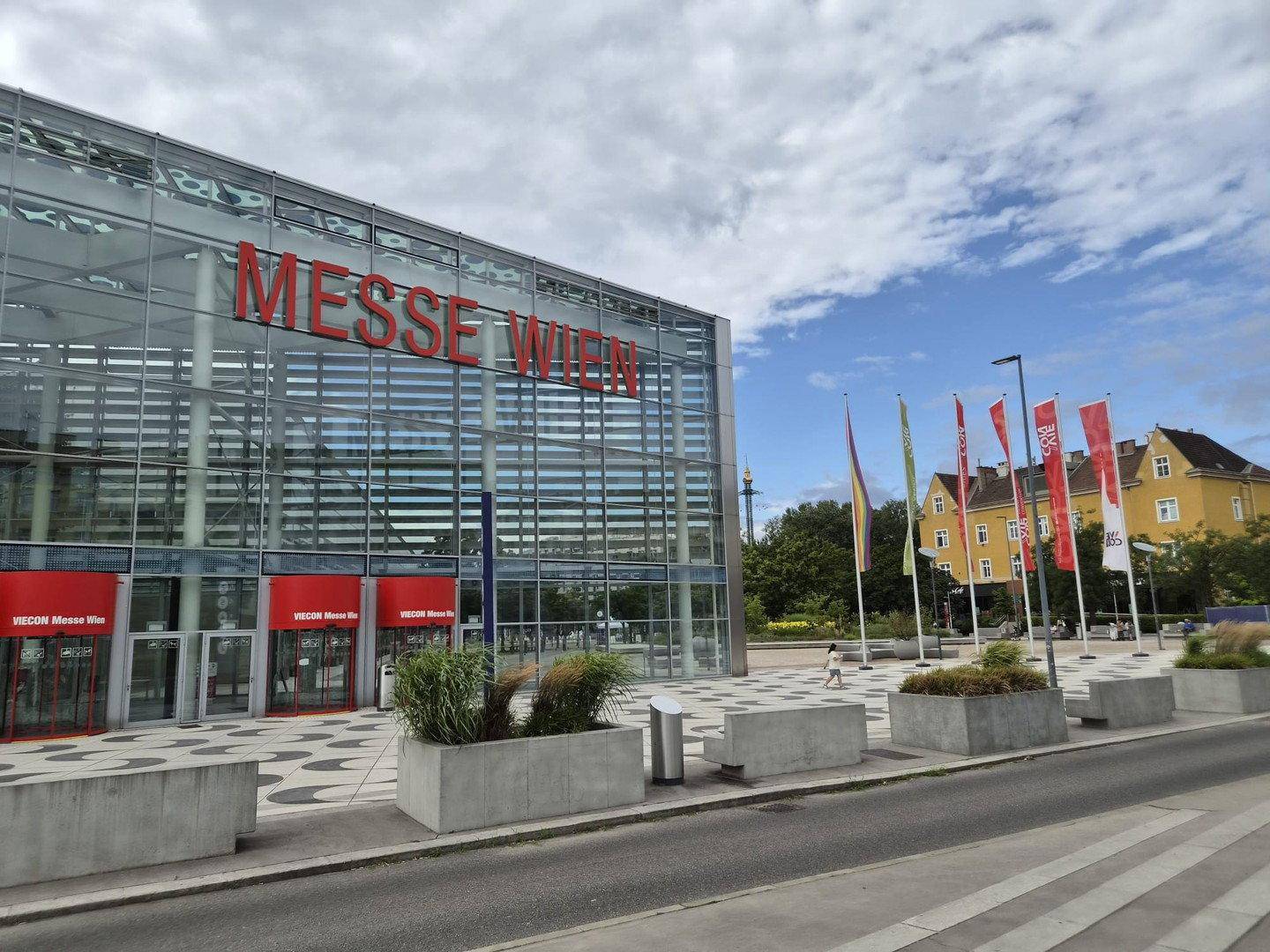 Moderne Glasfassade der Messe Wien mit roten Akzenten und Fahnen unter blauem Himmel.