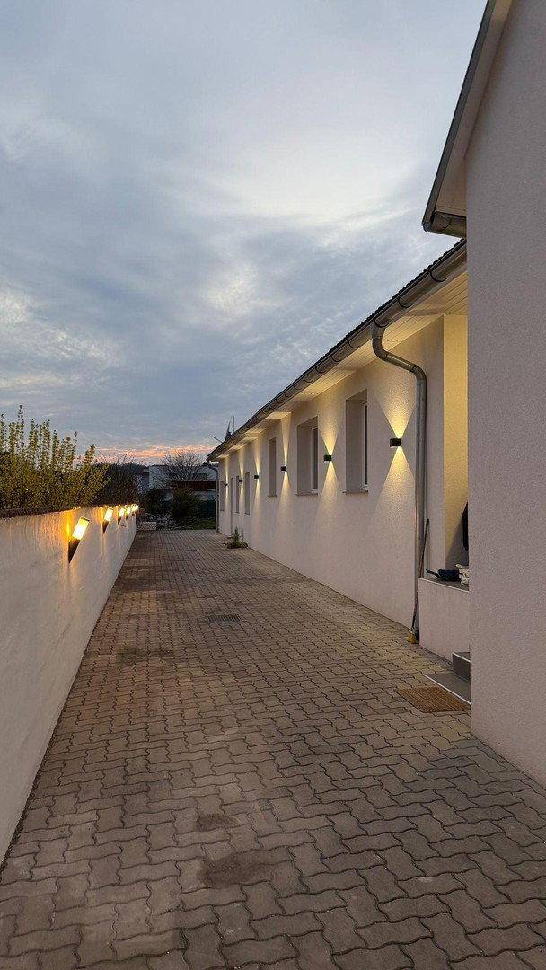 Beleuchteter Außenbereich des Gebäudes bei Dämmerung mit gepflastertem Weg und Gartenbeleuchtung.
