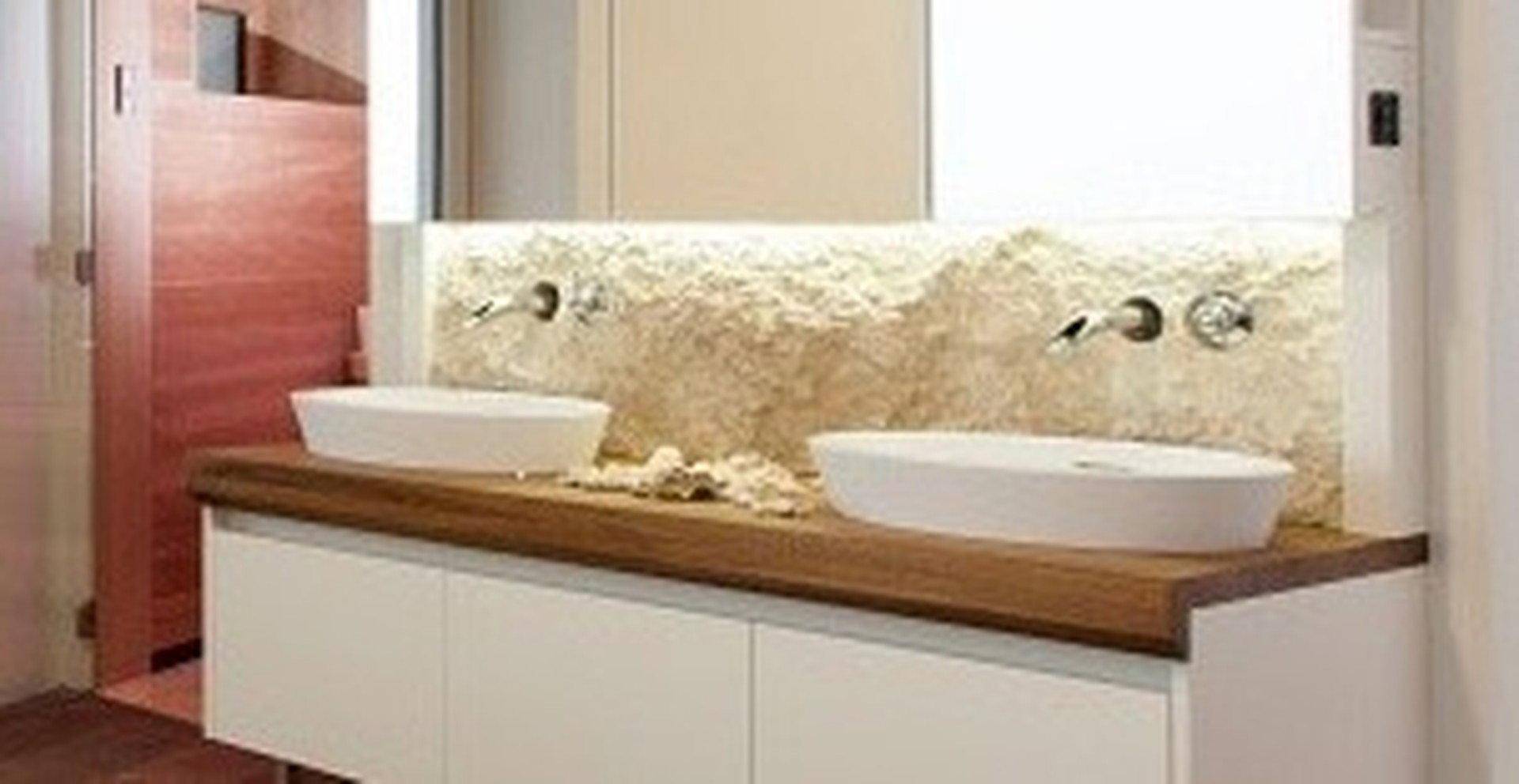 Modernes Badezimmer mit Doppelwaschbecken, Holzplatte und einer dekorativen Natursteinwand.