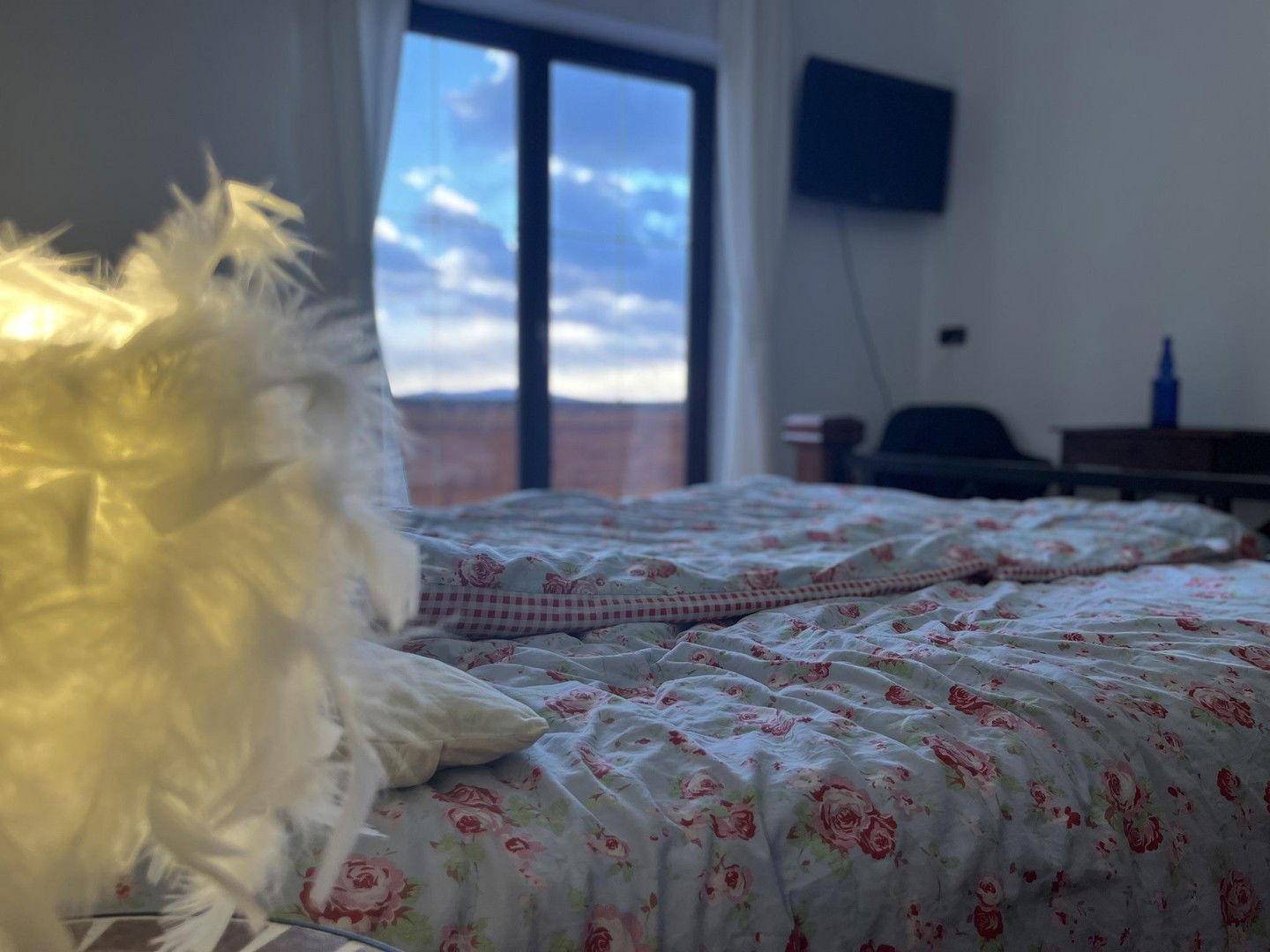 Gemütliches Schlafzimmer mit floraler Bettwäsche und Blick auf den Himmel durch die Balkontür.