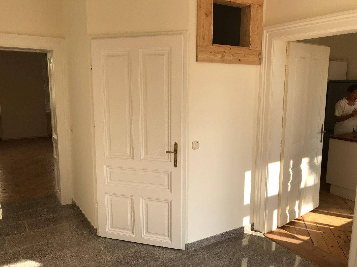 Heller Flurbereich mit Fliesenboden, weißen Türen und einem dekorativen Holzelement an der Wand.