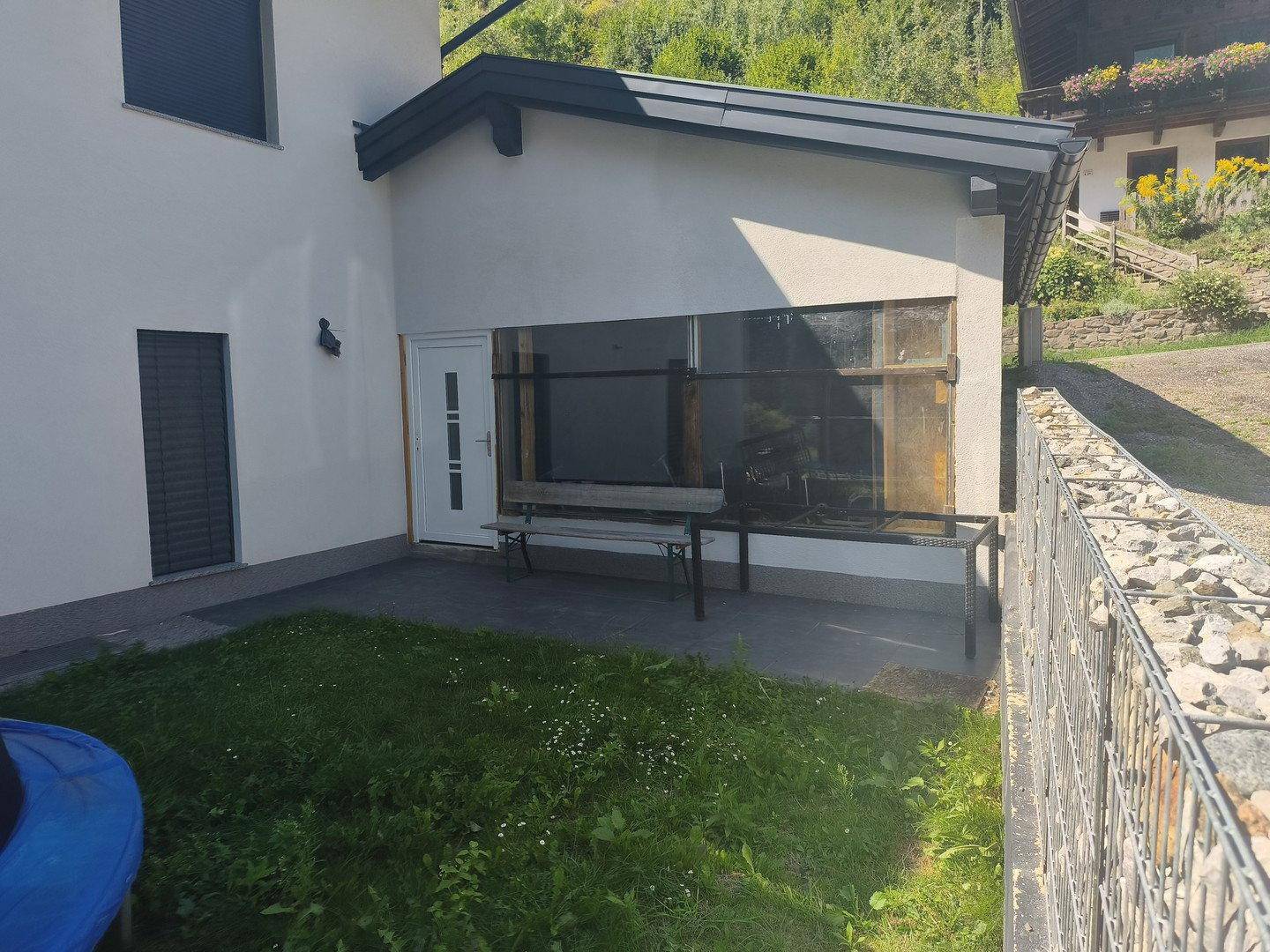 Kleiner Terrassenbereich am Haus mit einer Bank und Gabionenmauer im Vordergrund.