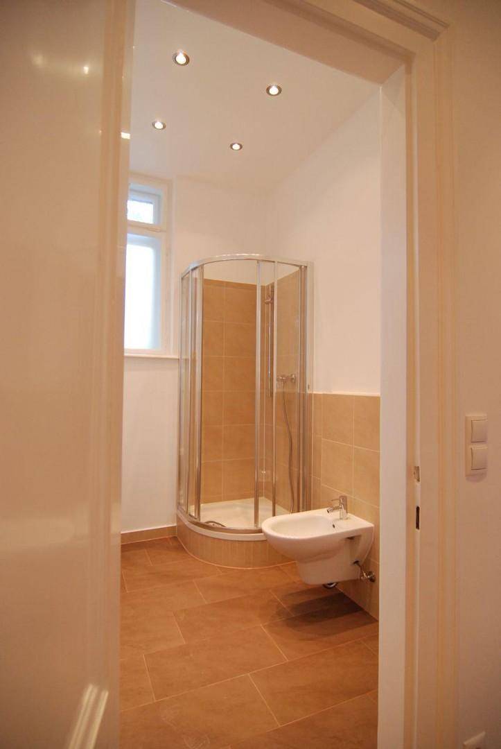 Badezimmer mit Duschkabine, Bidet, beigefarbenen Fliesen und kleinem Fenster.