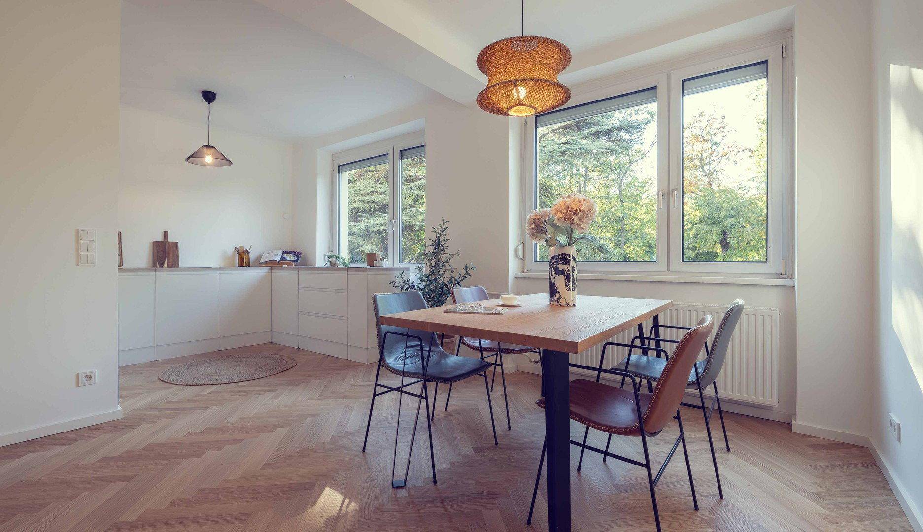Heller Essbereich mit Holztisch, modernen Stühlen und integrierter Küchenzeile im Hintergrund.