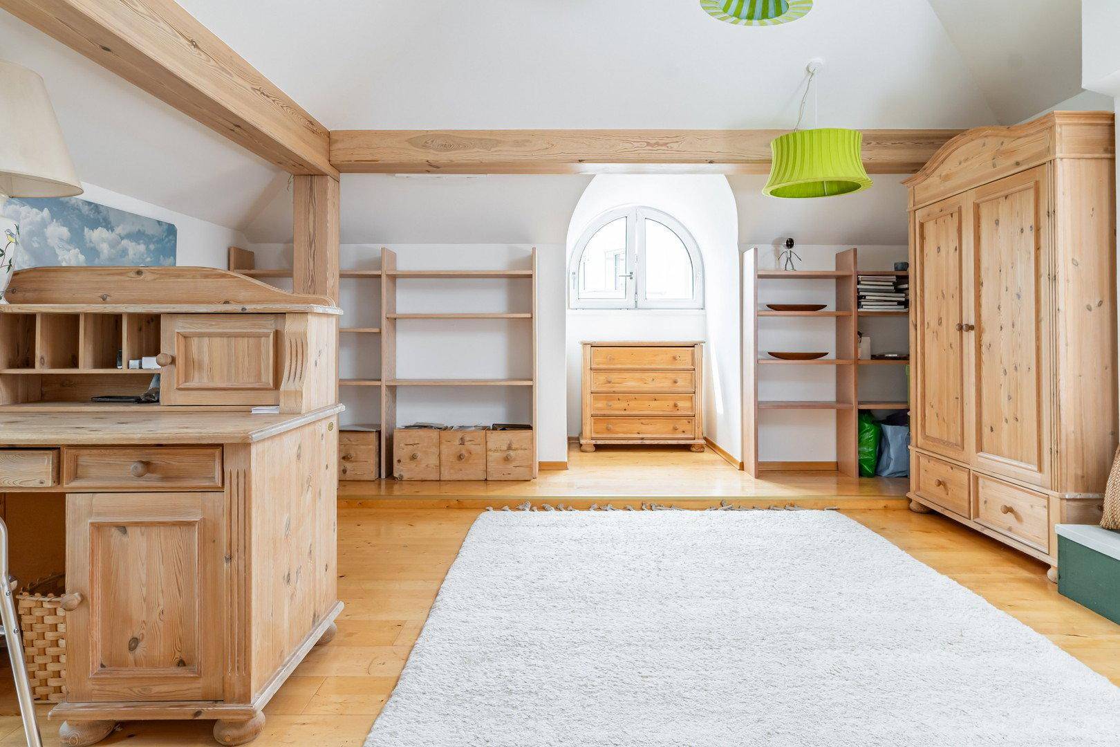 Helles Dachzimmer mit Holzbalken, Holzboden und rustikalen Holzmöbeln.